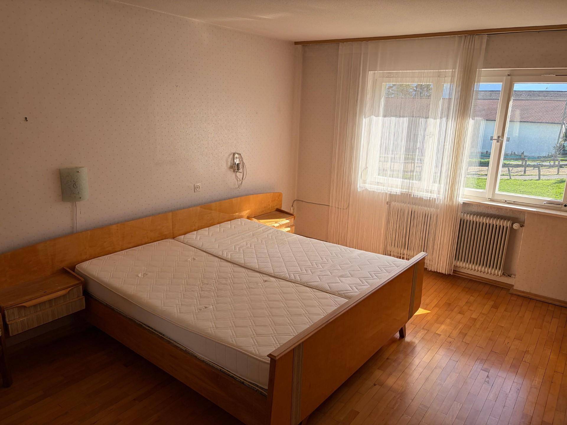 Helles Schlafzimmer mit Doppelbett, Holzfußboden und Blick ins Grüne.