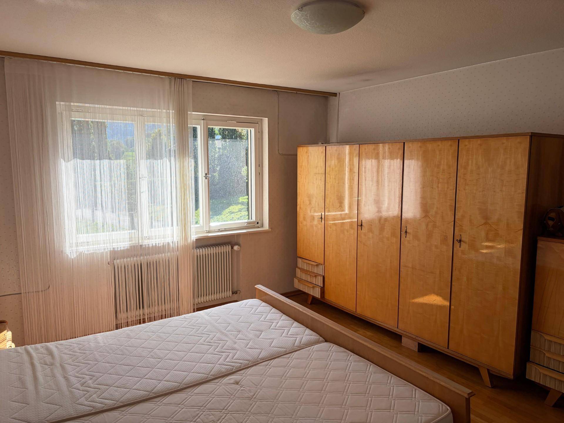 Schlafzimmer mit Holzschrank, Doppelbett und Fenster mit Blick auf die Umgebung.