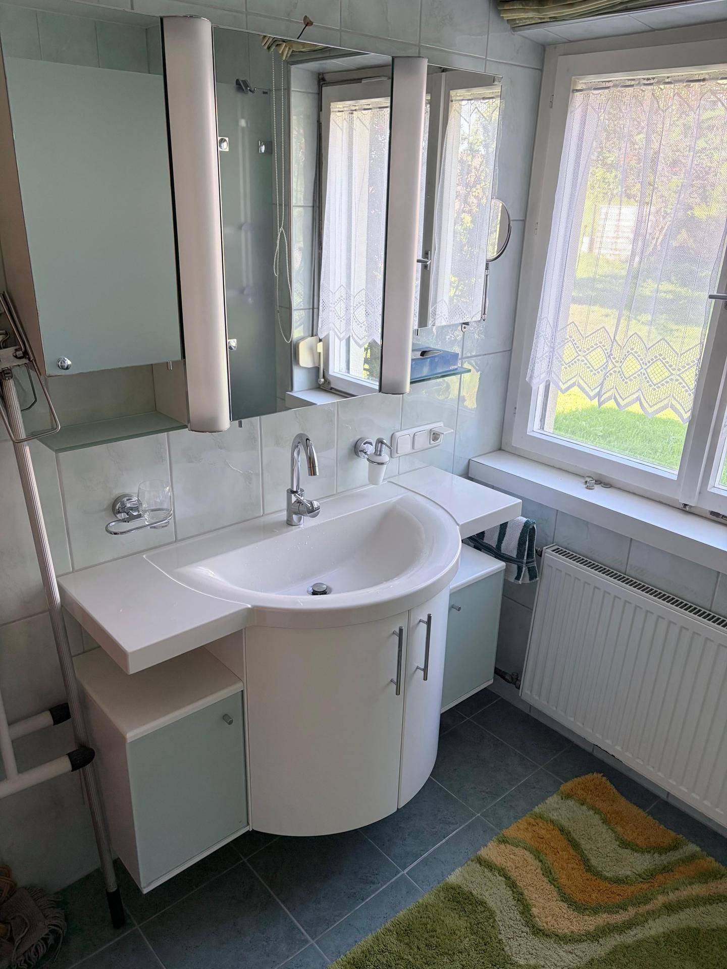 Badezimmer mit Waschtisch, Spiegelschrank und Fenster für Tageslicht.