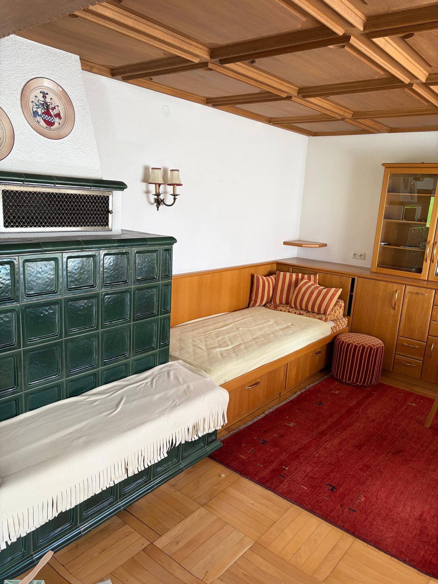 Detailansicht des traditionellen Kachelofens und einer gemütlichen Sitzecke im Wohnbereich.