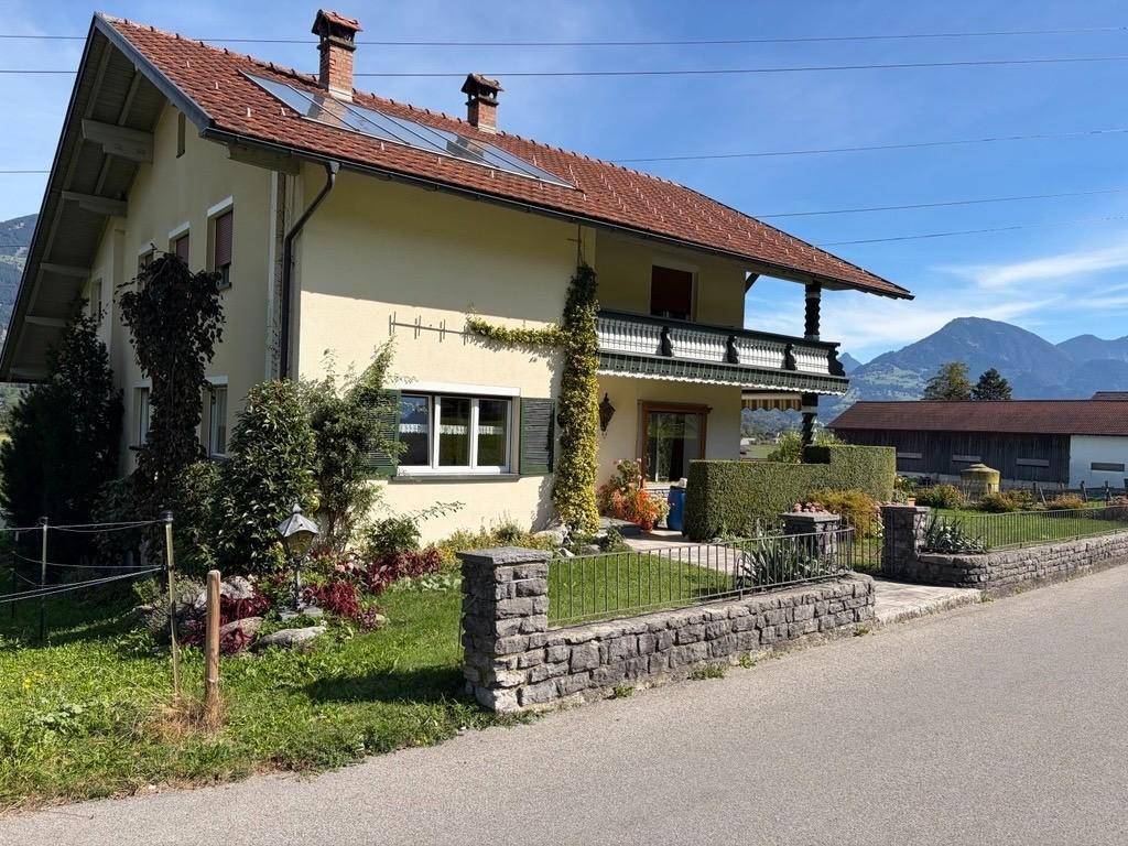 Rückansicht des Hauses mit Solarpaneelen auf dem Dach und Bergblick im Hintergrund.