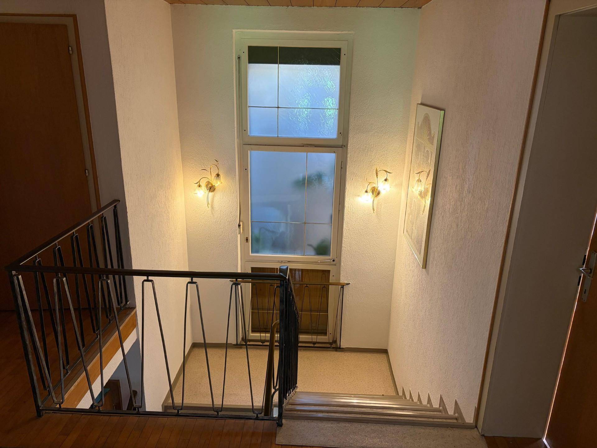 Treppenhaus mit schmiedeeisernem Geländer und Fenster für natürliches Licht.