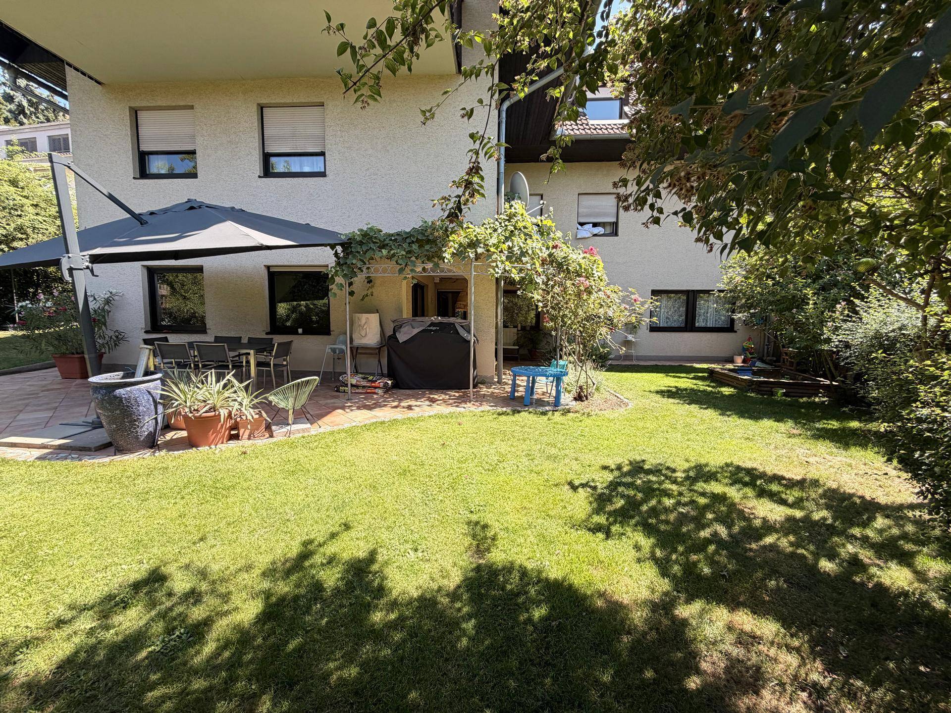 Rückseite des Hauses mit großer Terrasse, Essbereich im Freien und weitläufigem Rasen.