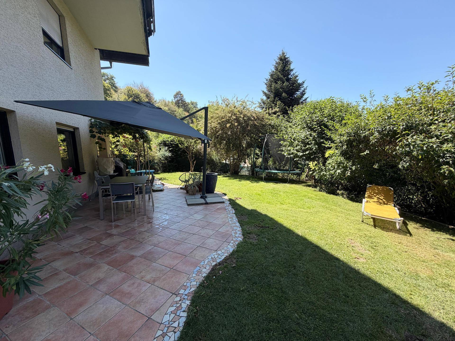 Sonnige Terrasse mit Essbereich und großem Garten mit Trampolin für Freizeitaktivitäten.