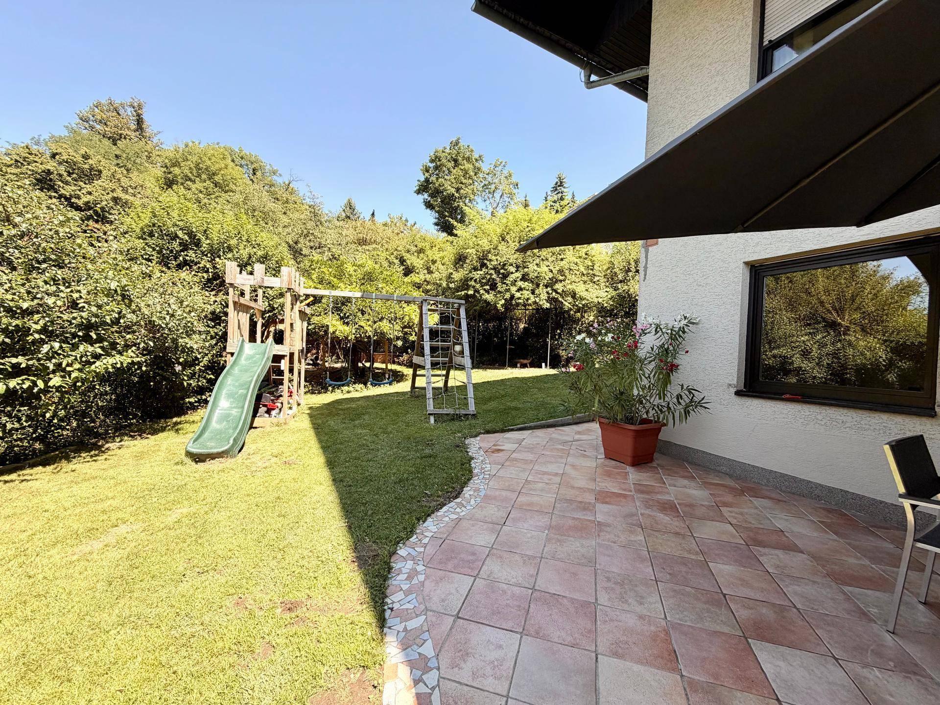 Gepflegter Garten mit großer Terrasse, Spielplatz und viel Grünfläche für Kinder.