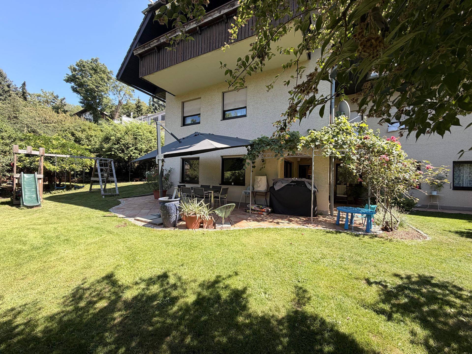 Weitläufiger Gartenbereich mit Terrasse, Essplatz und Spielgeräten im Hintergrund.