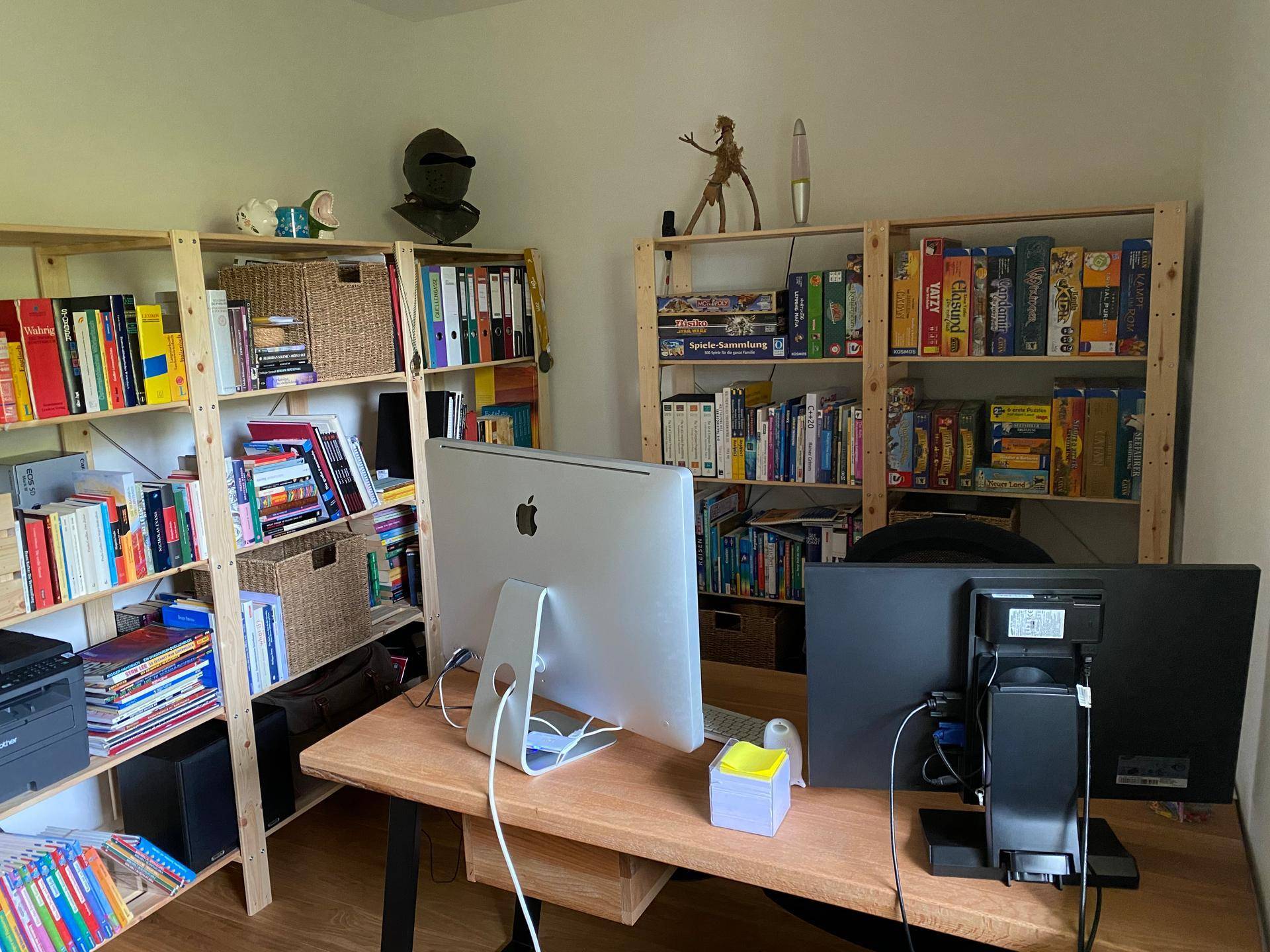 Funktionales Büro mit mehreren Bücherregalen, großem Schreibtisch und zwei Monitoren.
