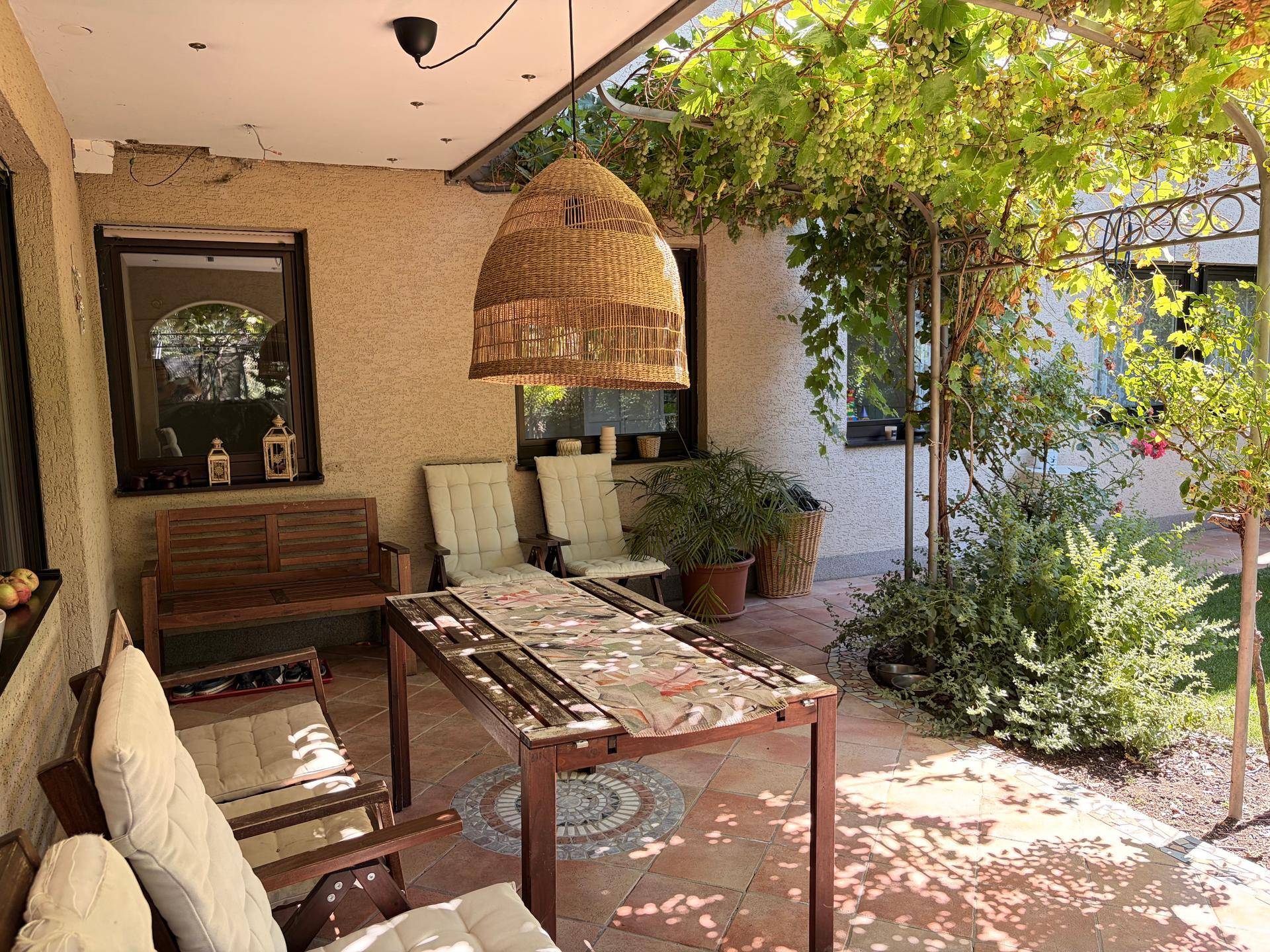 Überdachte Terrasse mit Gartenmöbeln, Hängelampe und üppiger Begrünung.