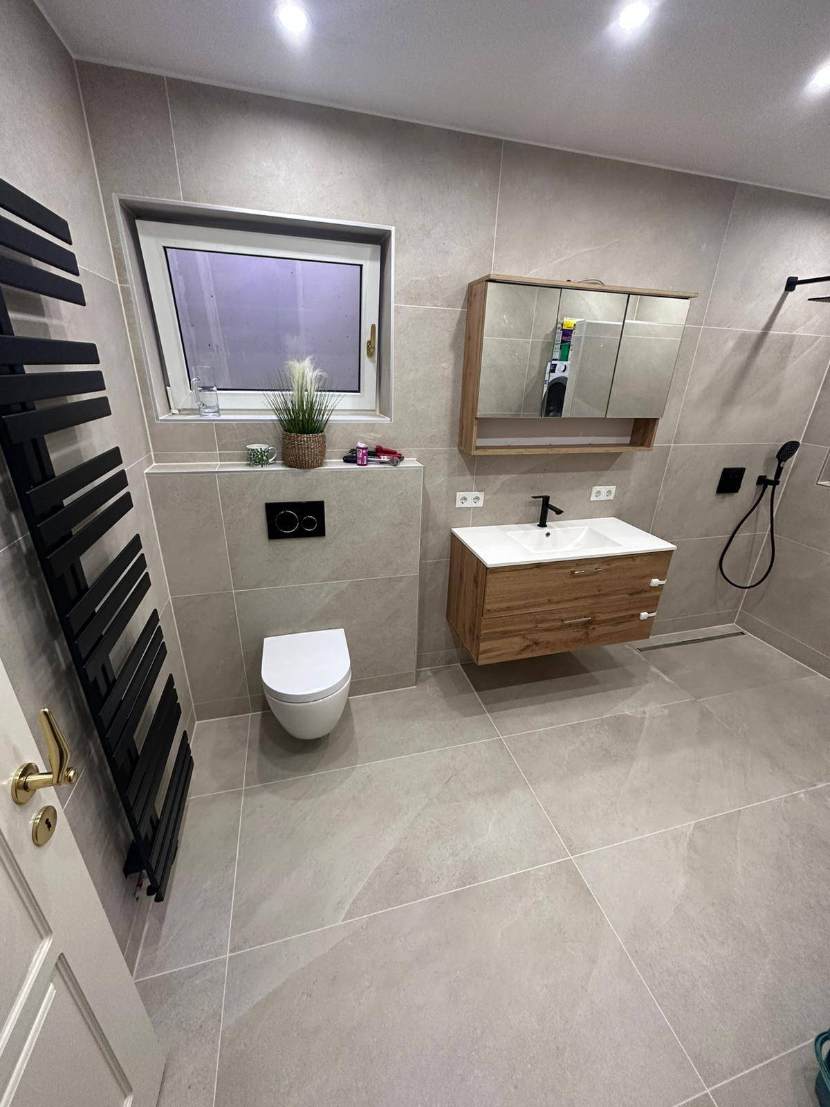 Modernes Badezimmer mit grauen Fliesen, schwebendem Waschtisch und beheiztem Handtuchhalter.