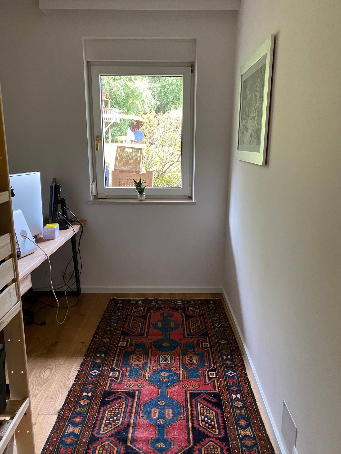 Kleiner Arbeitsbereich mit Schreibtisch, Computer und Fenster mit Blick ins Grüne.