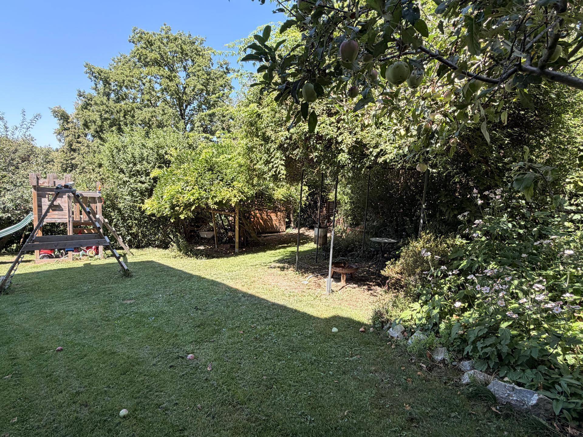 Weitläufiger Garten mit Spielplatz, Schaukeln und einer Vielfalt an Bäumen und Pflanzen.