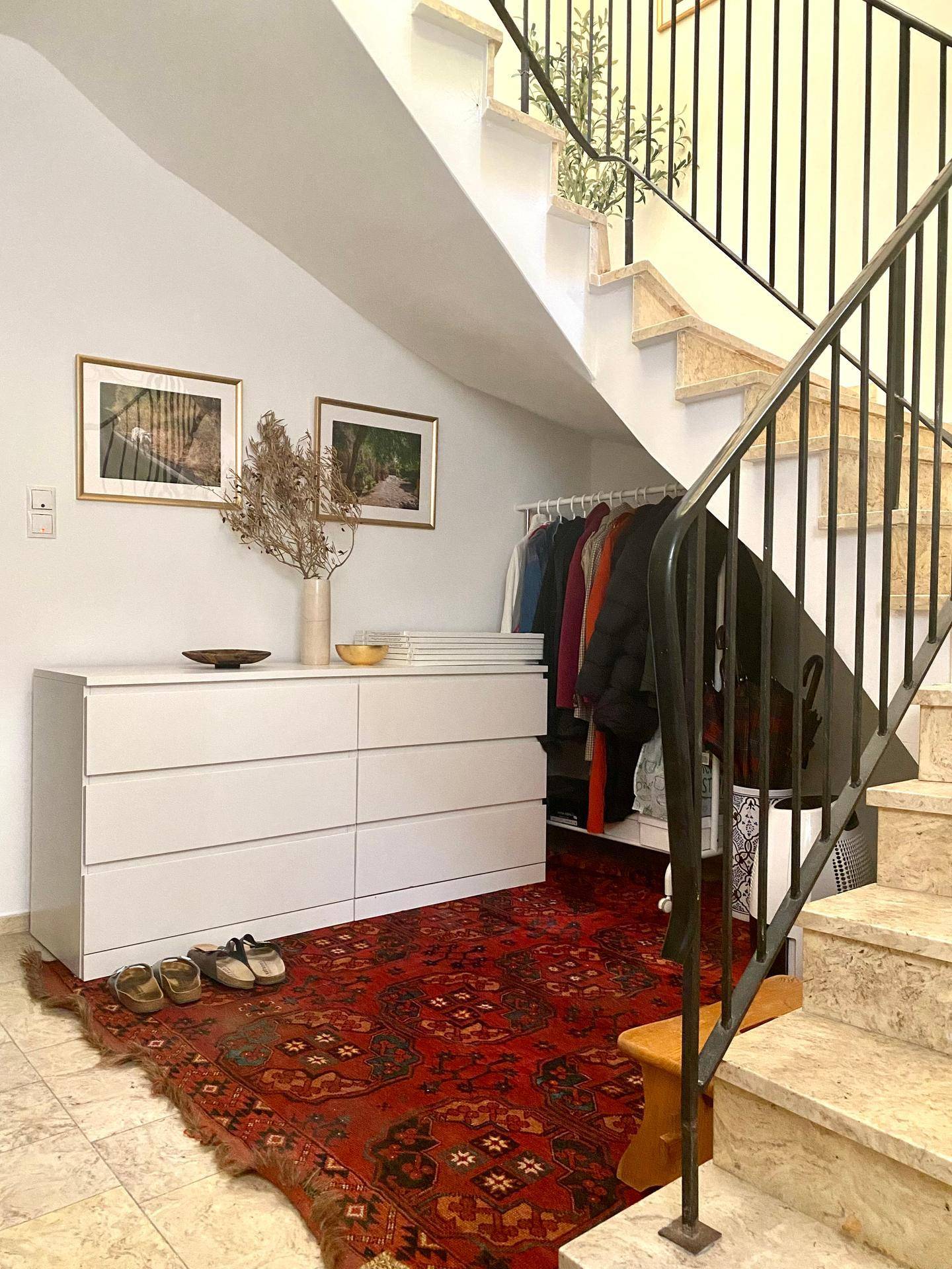 Eingangsbereich unter der Treppe mit Kommode, Teppich und Garderobenstange.