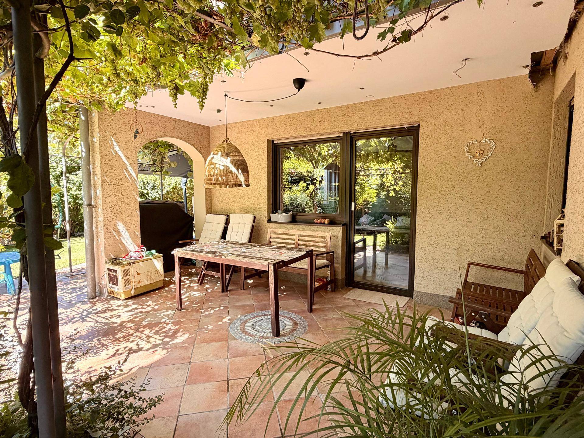 Überdachte Terrasse mit Fliesenboden, gemütlichen Sitzgelegenheiten und Zugang zum Garten.