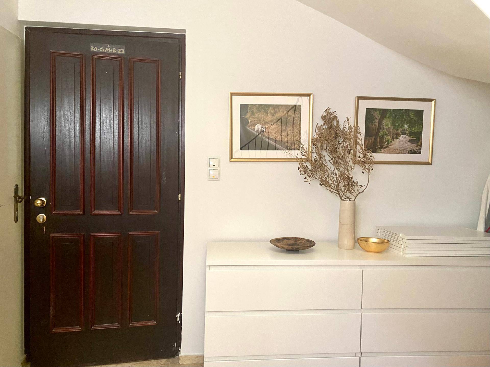 Dunkle Eingangstür neben einer weißen Kommode und gerahmten Bildern an der Wand.