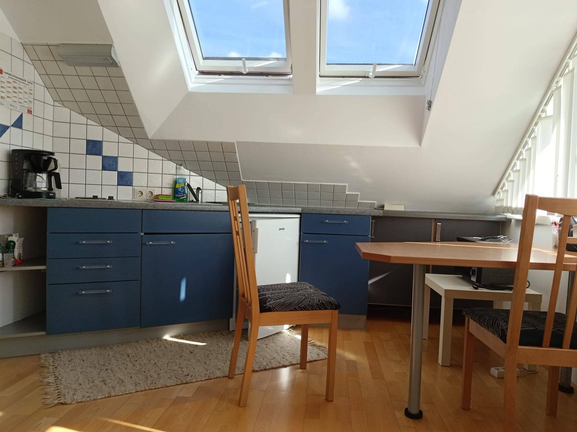 Funktionale Küche mit blauen Unterschränken, Esstisch und Dachfenstern für viel natürliches Licht.