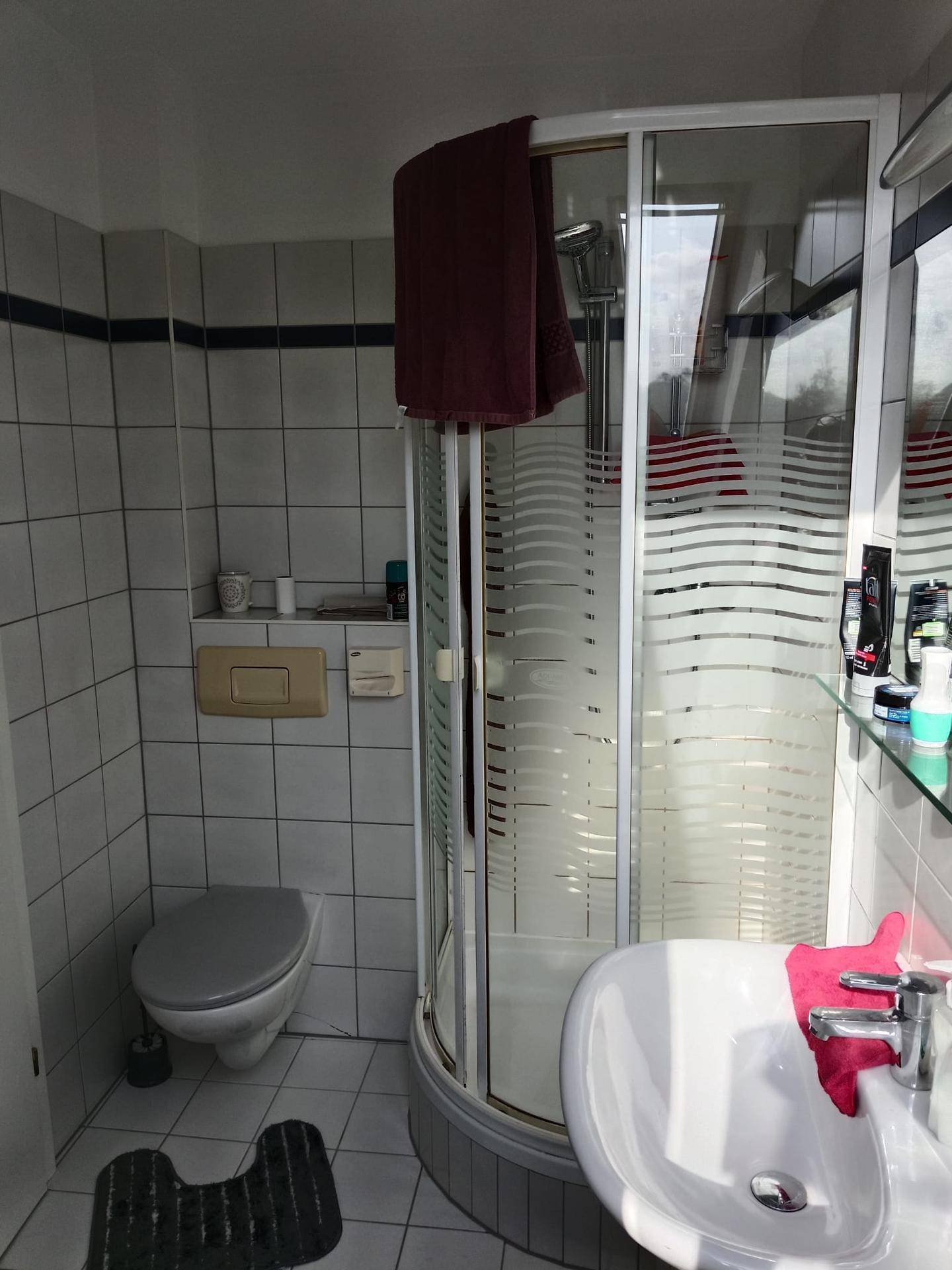 Badezimmer mit Duschkabine, wandhängender Toilette und Waschbecken, gefliest in Weiß und Grau.