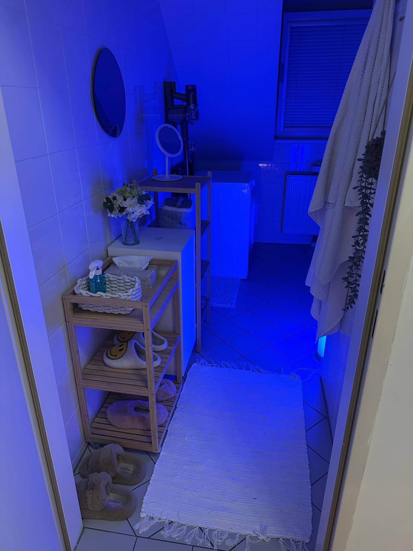 Badezimmer mit blauer Beleuchtung, Spiegelschrank und Ablageregalen unter einer Dachschräge.