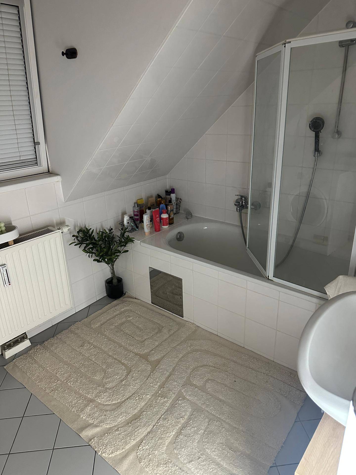 Helles Badezimmer unter einer Dachschräge mit Badewanne, Duschabtrennung und Fenster.