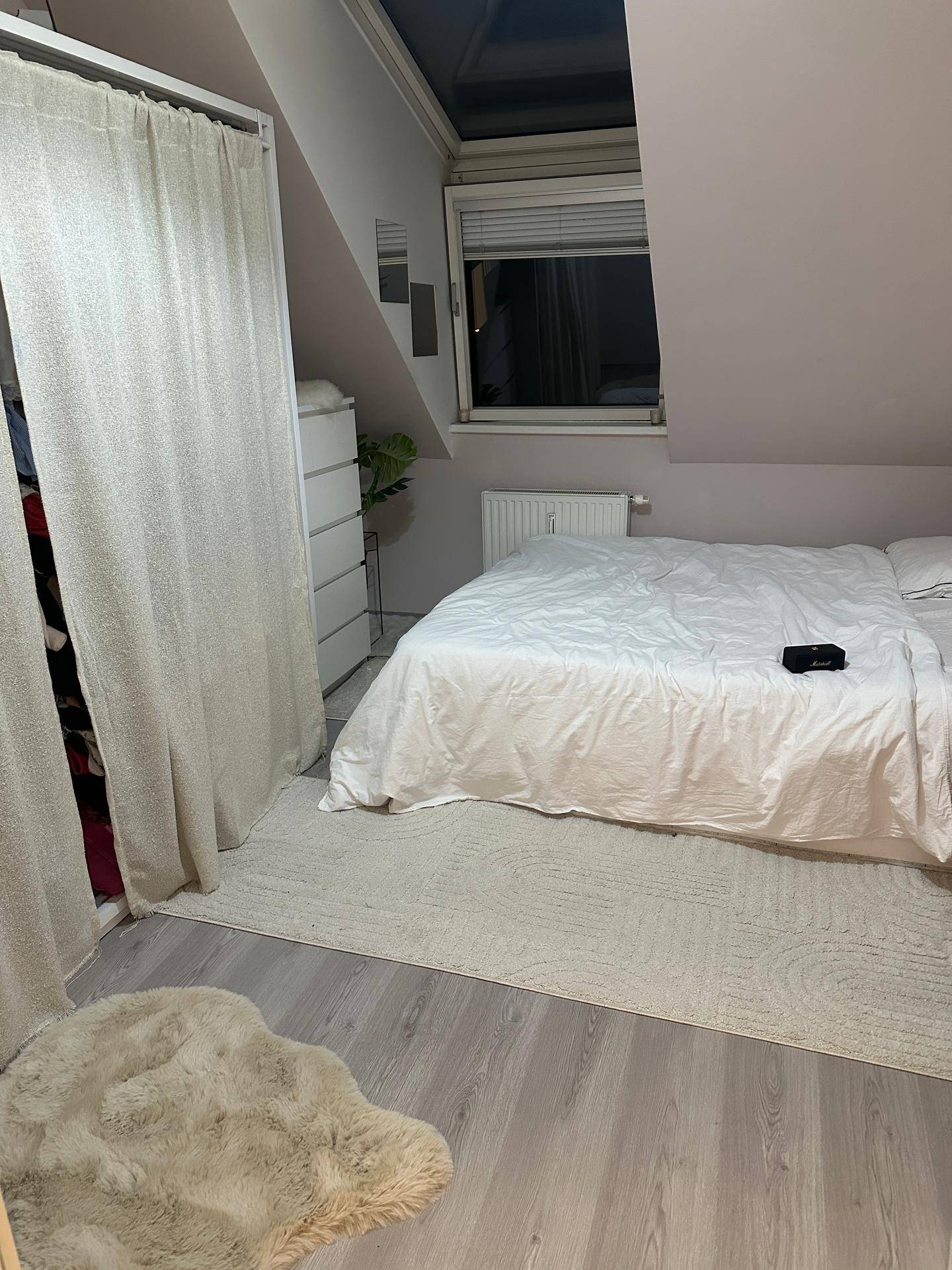 Schlafzimmer mit Doppelbett, Kleiderschrank und Dachfenster, das für natürliches Licht sorgt.