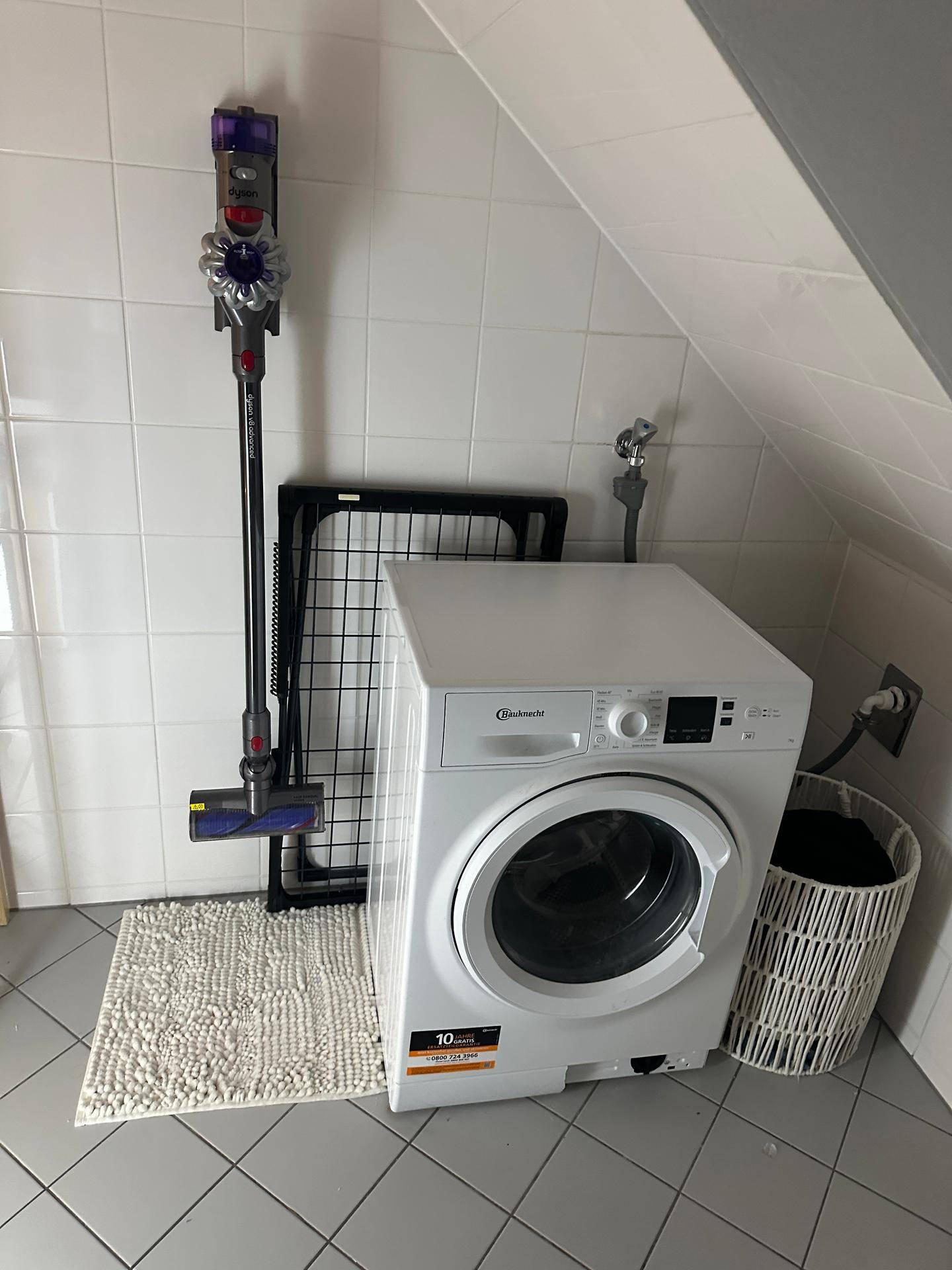 Waschbereich im Badezimmer mit Waschmaschine, Wäscheständer und Staubsauger unter der Dachschräge.