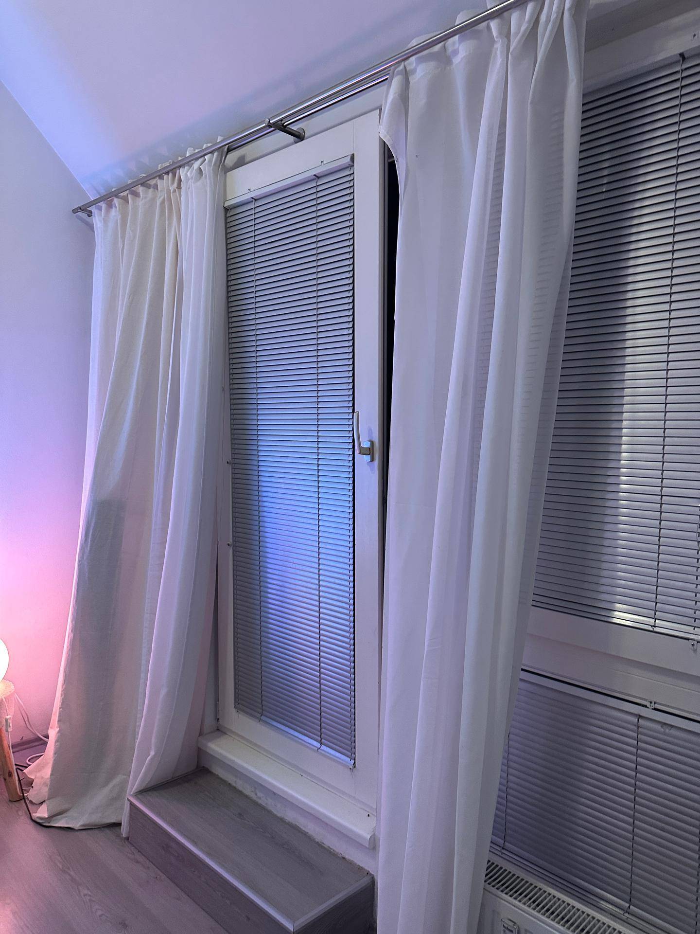 Französischer Balkon mit Vorhängen und Jalousien, der viel Licht in den Wohnbereich lässt.