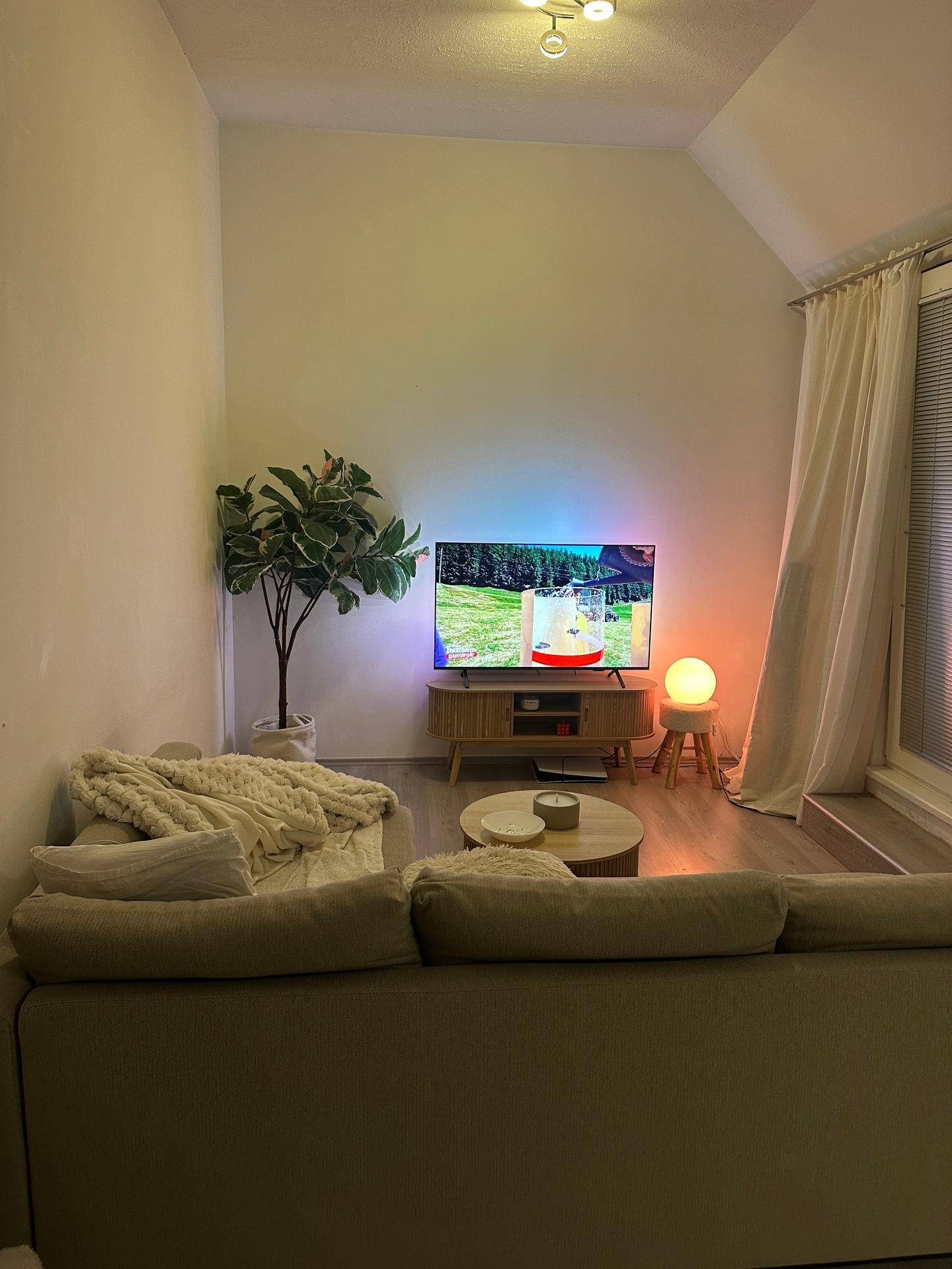 Gemütliches Wohnzimmer mit Sofa, Fernseher und dekorativer Beleuchtung unter einer Dachschräge.
