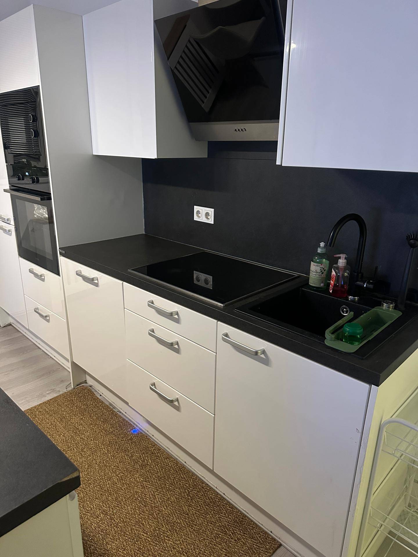 Moderne Küche mit Induktionskochfeld, Spüle und Dunstabzugshaube in Hochglanz-Optik.