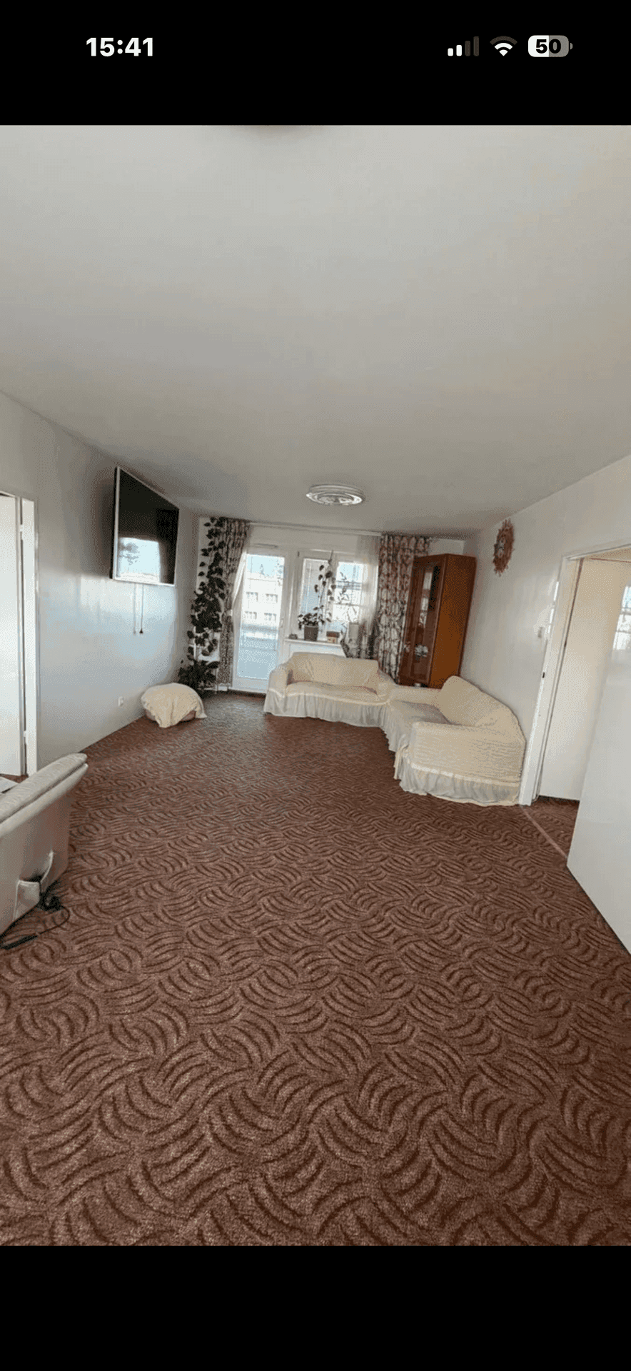 Geräumiges Wohnzimmer mit gemustertem Teppichboden, hellen Sofas und Zugang zum Balkon.