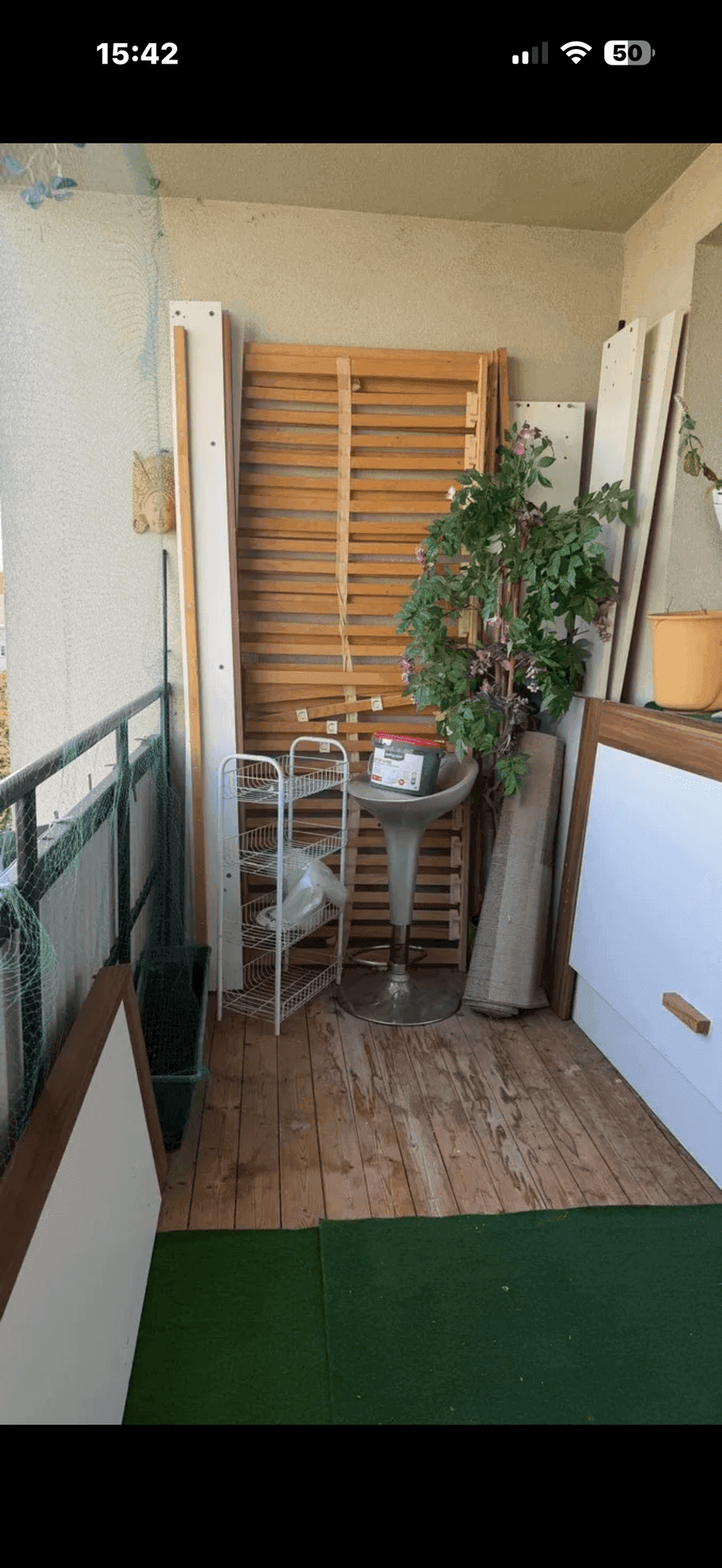 Balkon mit Holzboden, verschiedenen gelagerten Gegenständen und einer Pflanze.