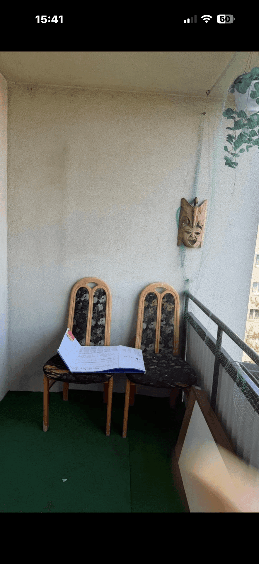 Balkon mit zwei Stühlen, einem kleinen Tisch und einer Holzmaske an der Wand.