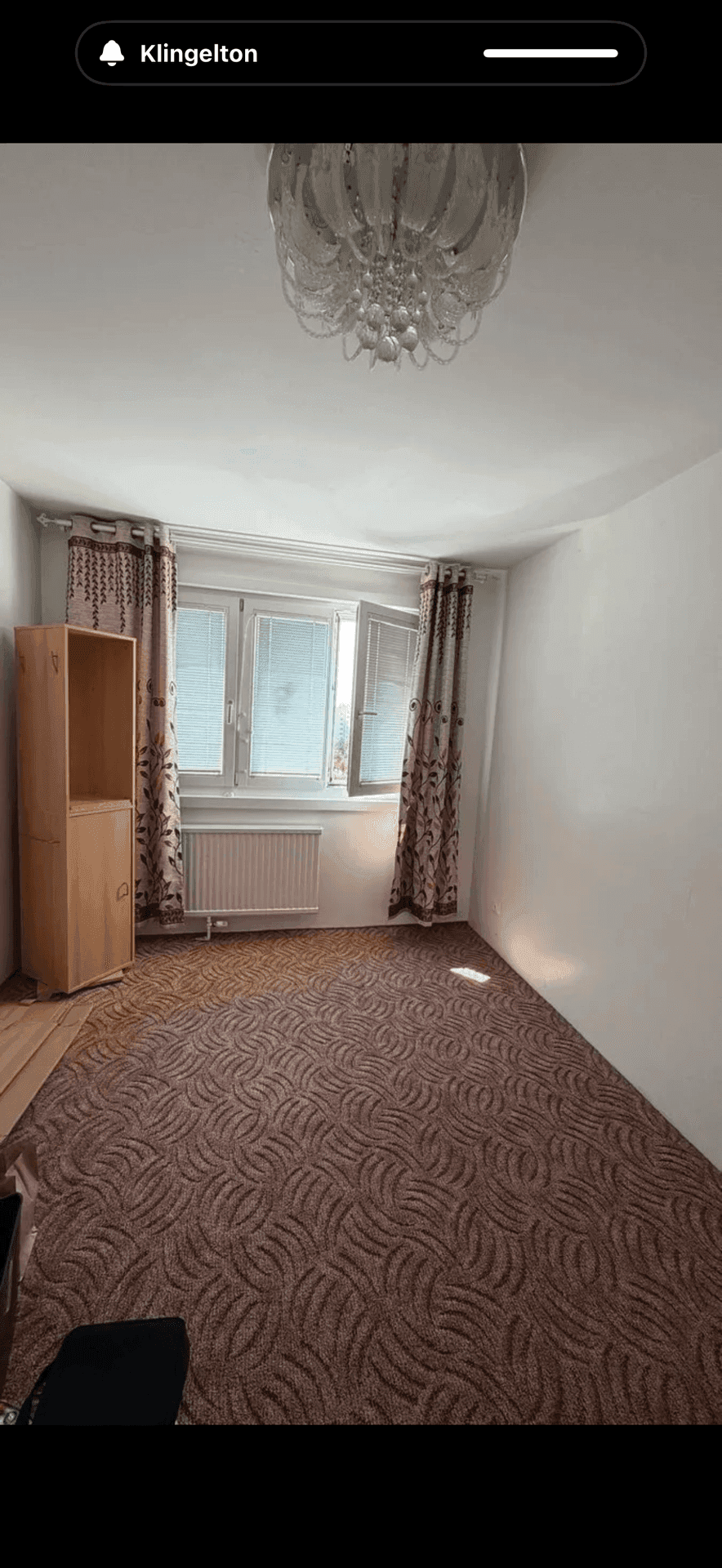 Schlafzimmer mit gemustertem Teppichboden, hellem Holzschrank und einem Fenster mit Tageslicht.