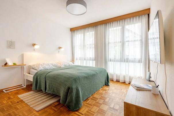 Gemütliches Schlafzimmer mit Doppelbett, Parkettboden und großen Fenstern für viel Tageslicht.