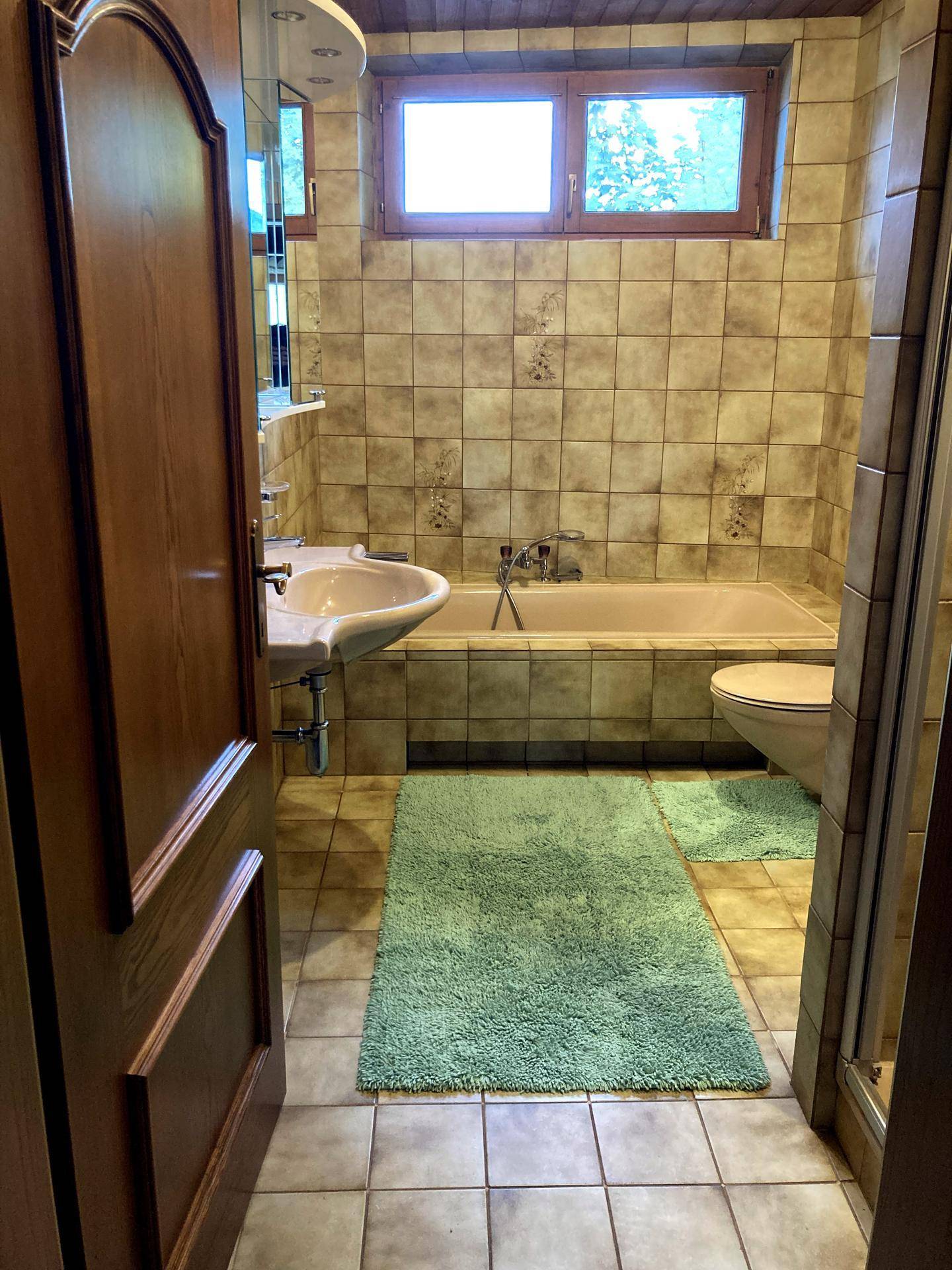 Traditionelles Badezimmer mit Badewanne, Waschbecken und WC, komplett gefliest in warmen Erdtönen.