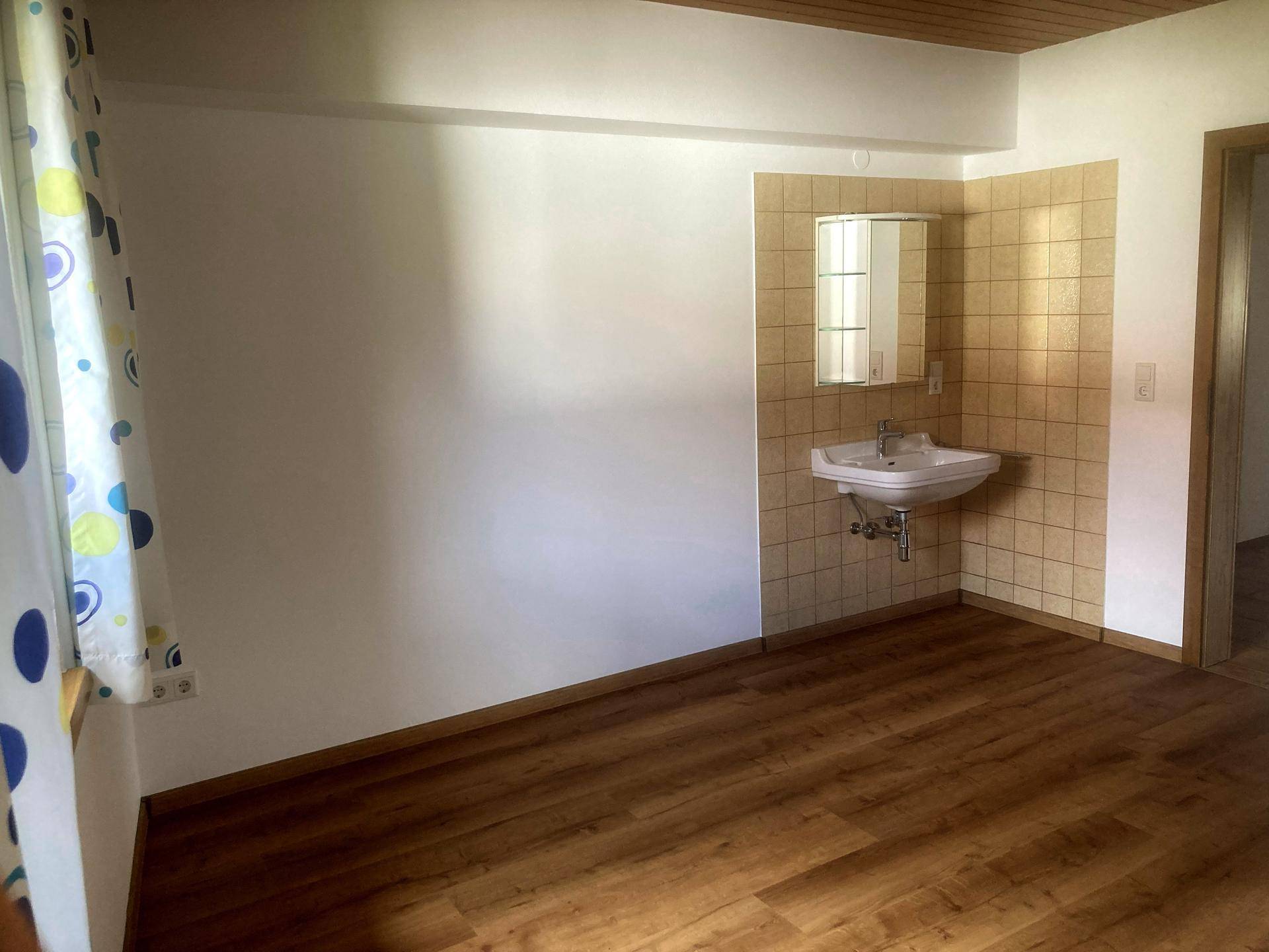 Heller Raum mit Laminatboden, Waschbecken und Spiegelschrank, der vielseitig genutzt werden kann.