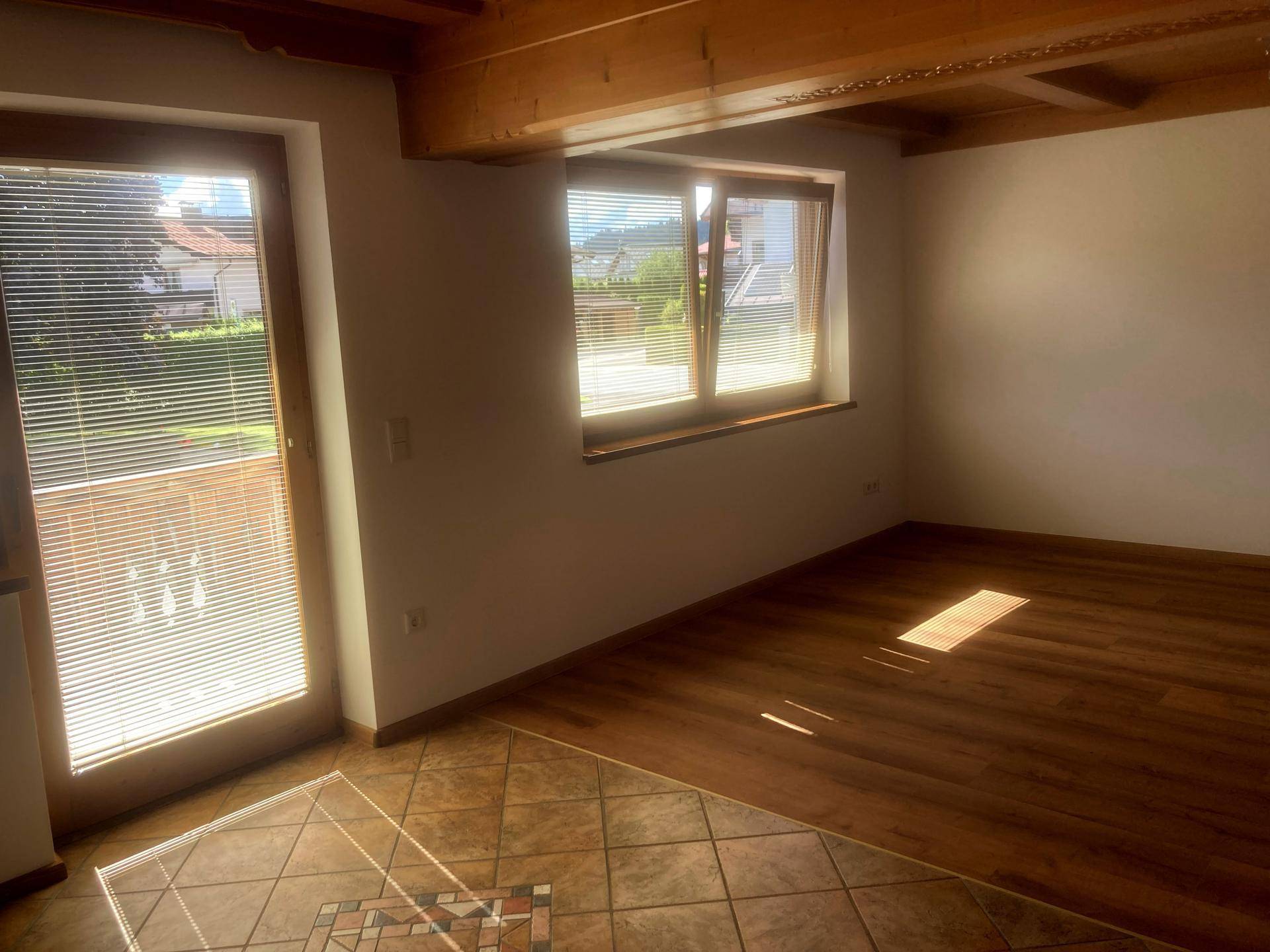 Heller Wohnbereich mit Laminatboden, Zugang zum Außenbereich und Blick ins Grüne durch die Fenster.