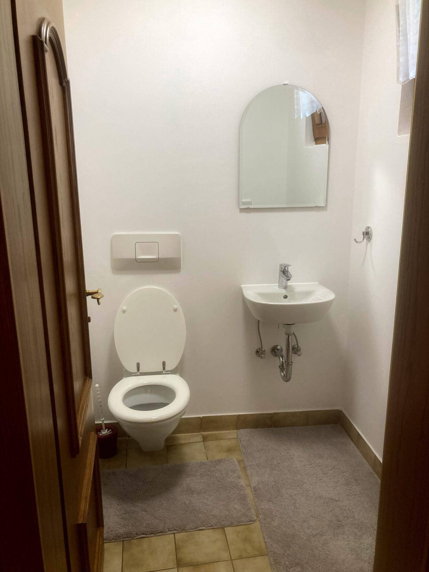 Kleines Gäste-WC mit modernem WC, Waschbecken und Spiegel, einfach und funktional gestaltet.