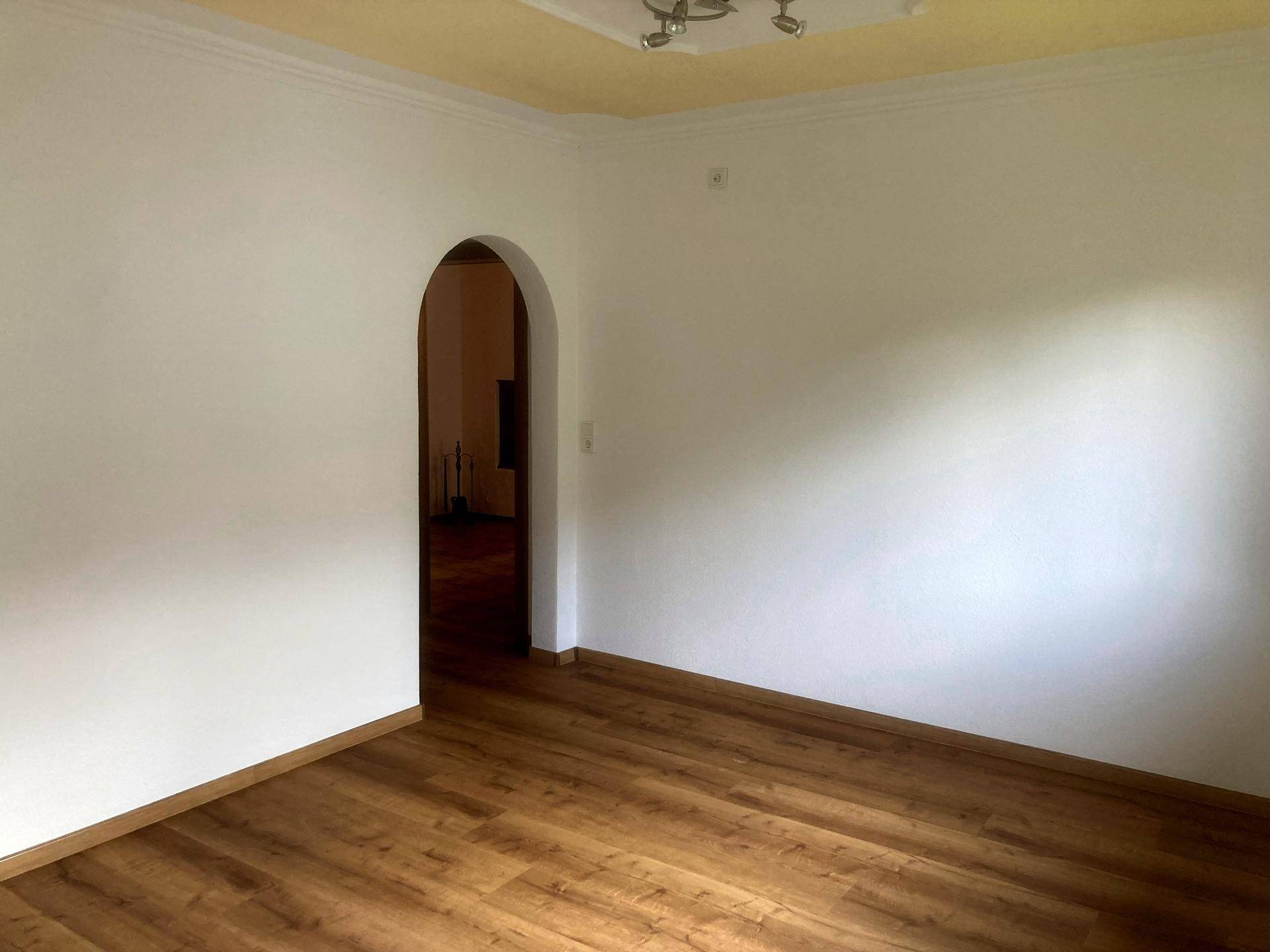 Geräumiger, heller Raum mit Laminatboden und einem Rundbogen, der zu einem weiteren Bereich führt.