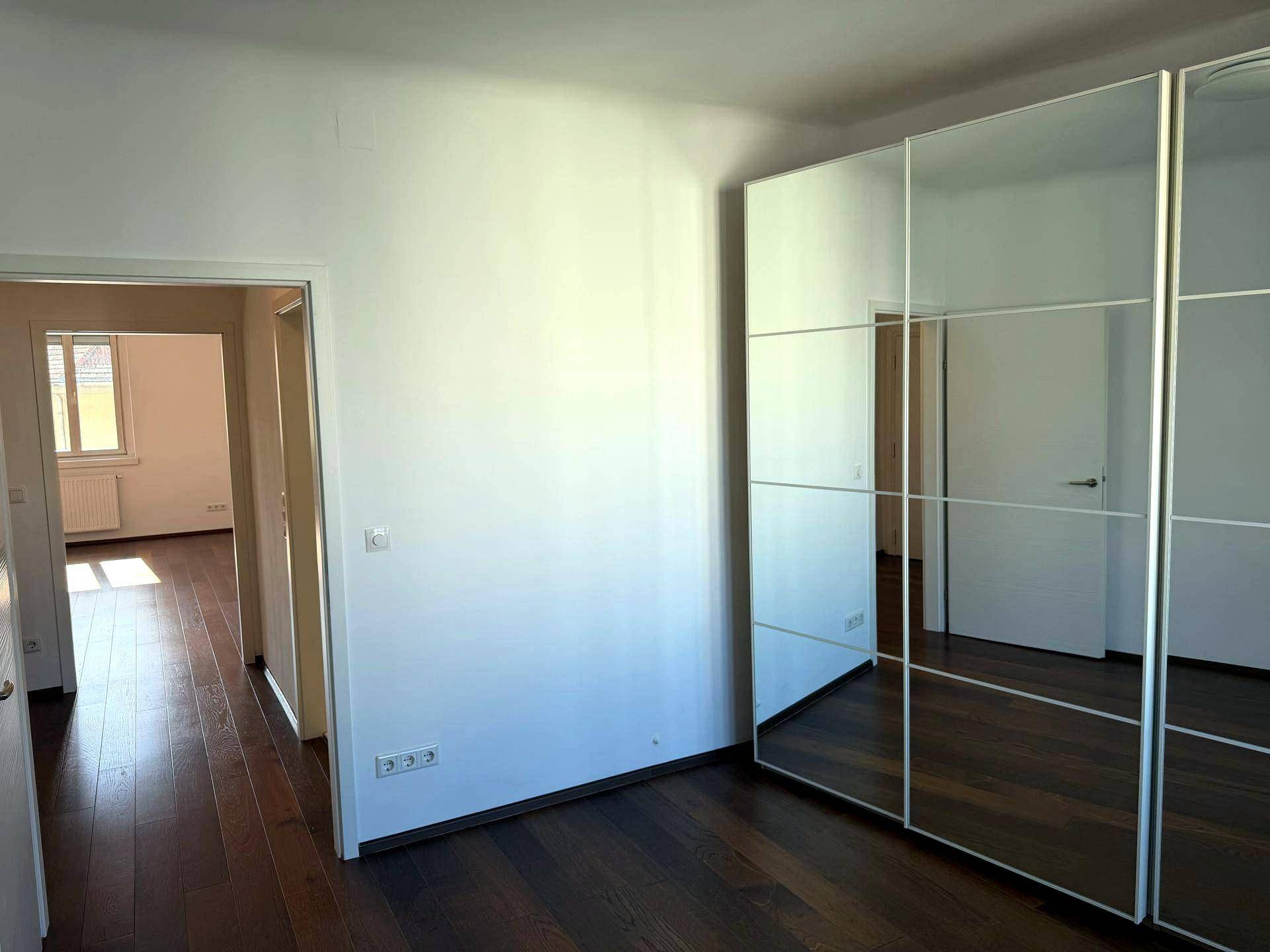 Schlafzimmer mit dunklem Holzboden und einem großen Spiegelschrank, der den Raum optisch vergrößert.
