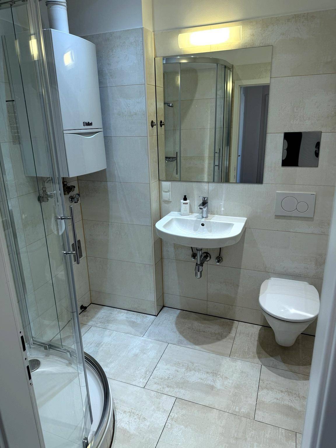 Modernes Badezimmer mit Duschkabine, Waschbecken und Toilette, hell gefliest.