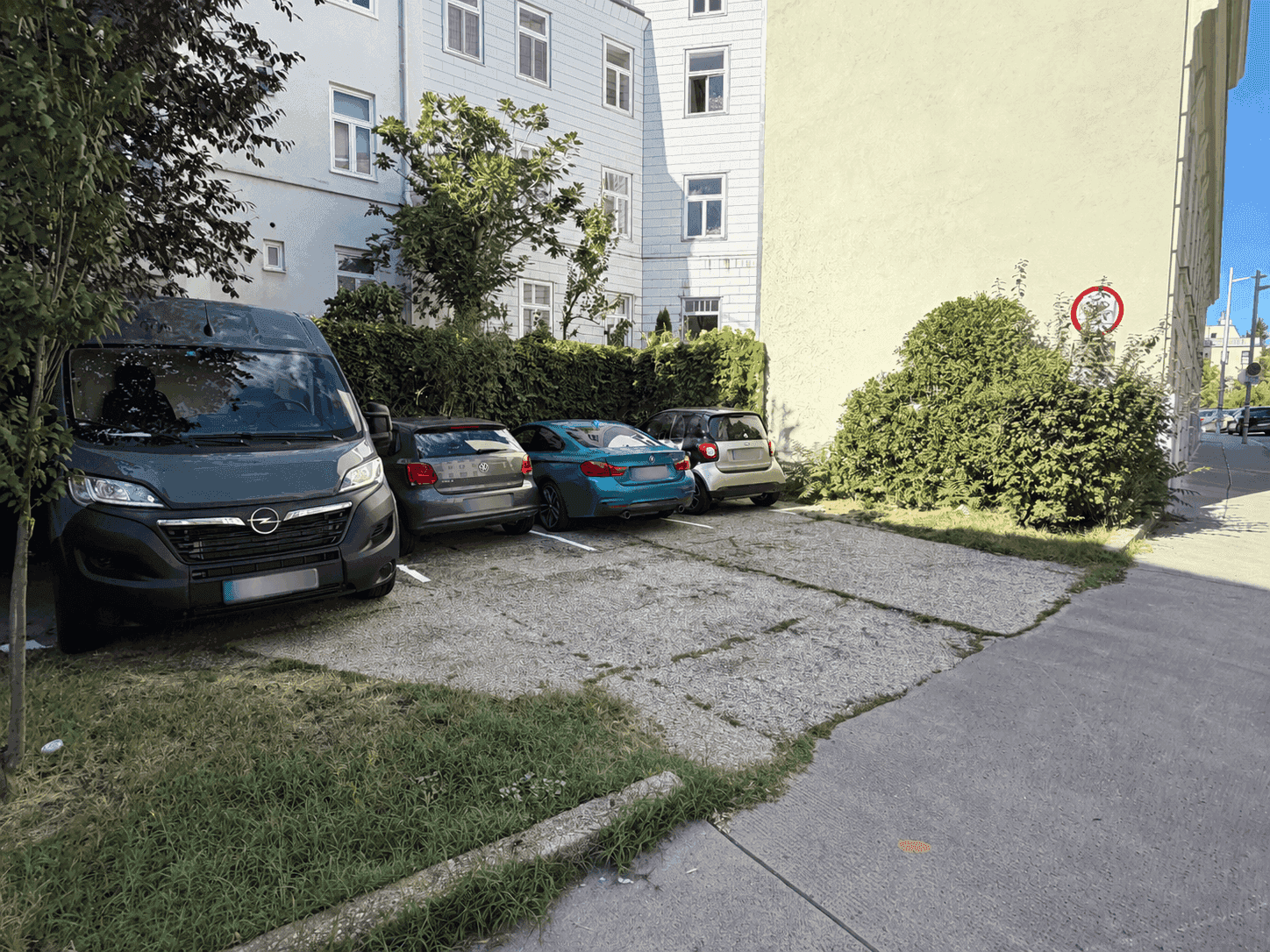 Außenparkplätze vor einem Gebäude mit mehreren geparkten Fahrzeugen und Grünflächen.