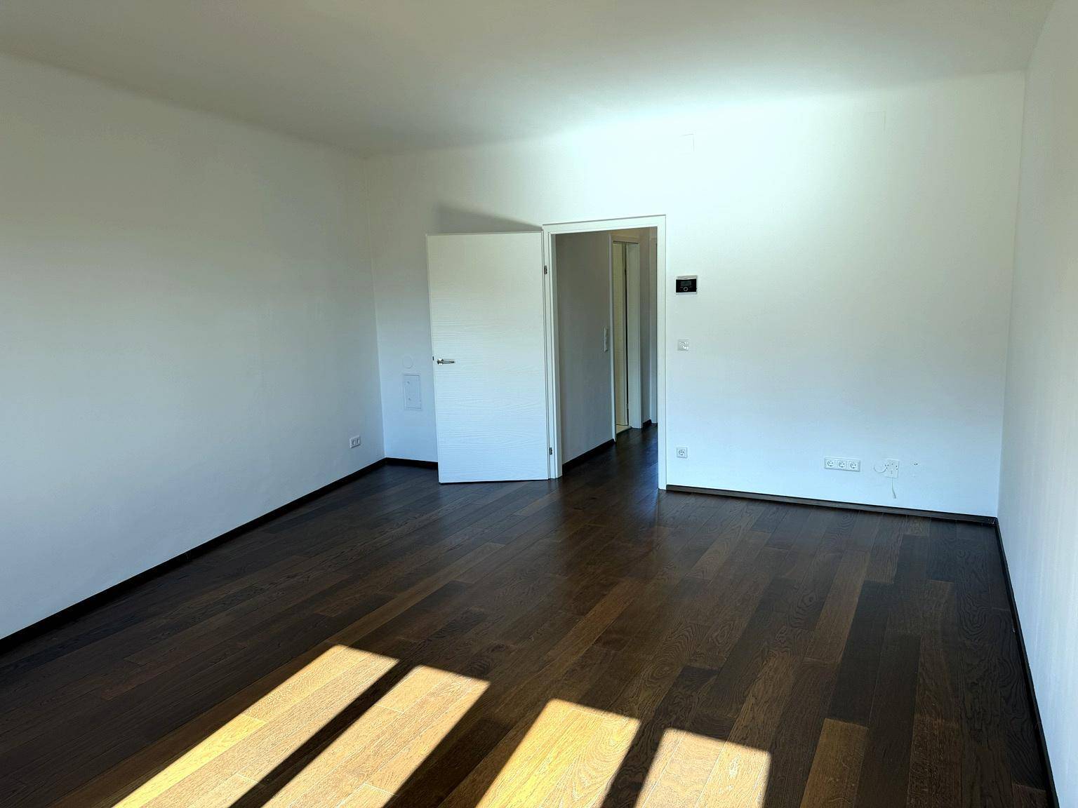 Geräumiger, heller Raum mit dunklem Holzboden und viel Tageslicht, ideal als Wohnbereich.