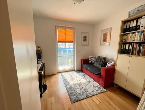 Helles Arbeitszimmer mit Zugang zum Balkon, Holzboden und Bücherregal.