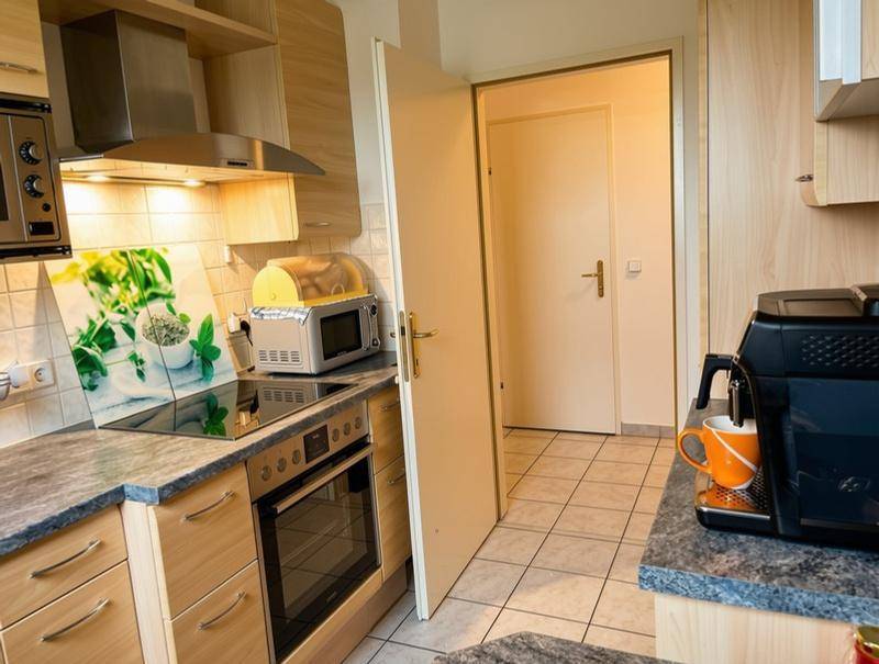 Funktionale Küche mit hellen Holzschränken, Fliesenboden und modernen Geräten.