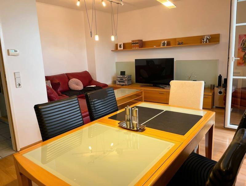 Heller Wohn- und Essbereich mit Holztisch, rotem Sofa und Parkettboden.