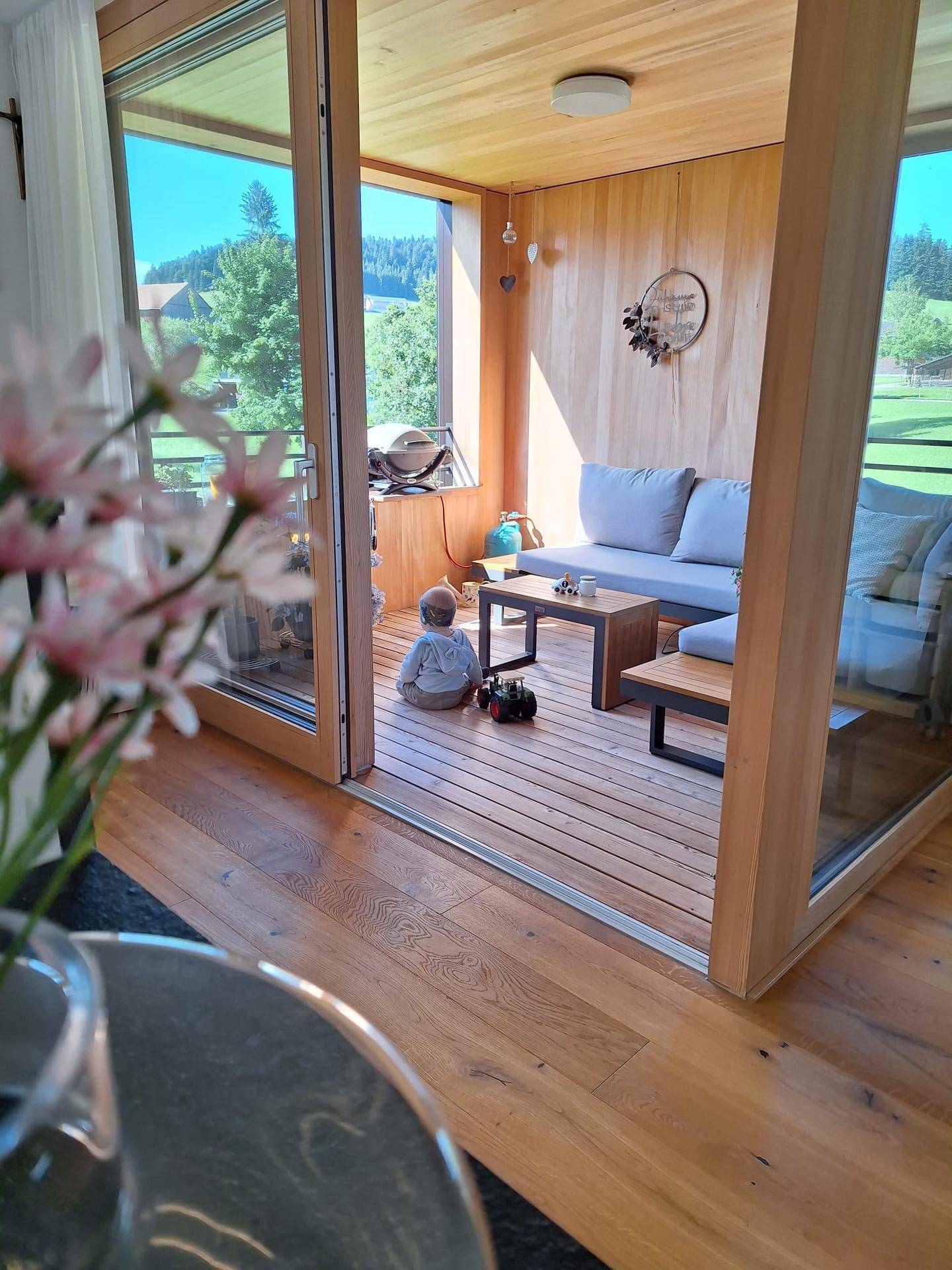 Gemütliche, verglaste Loggia mit Holzboden und Sitzgelegenheiten, ideal für Kinder zum Spielen.