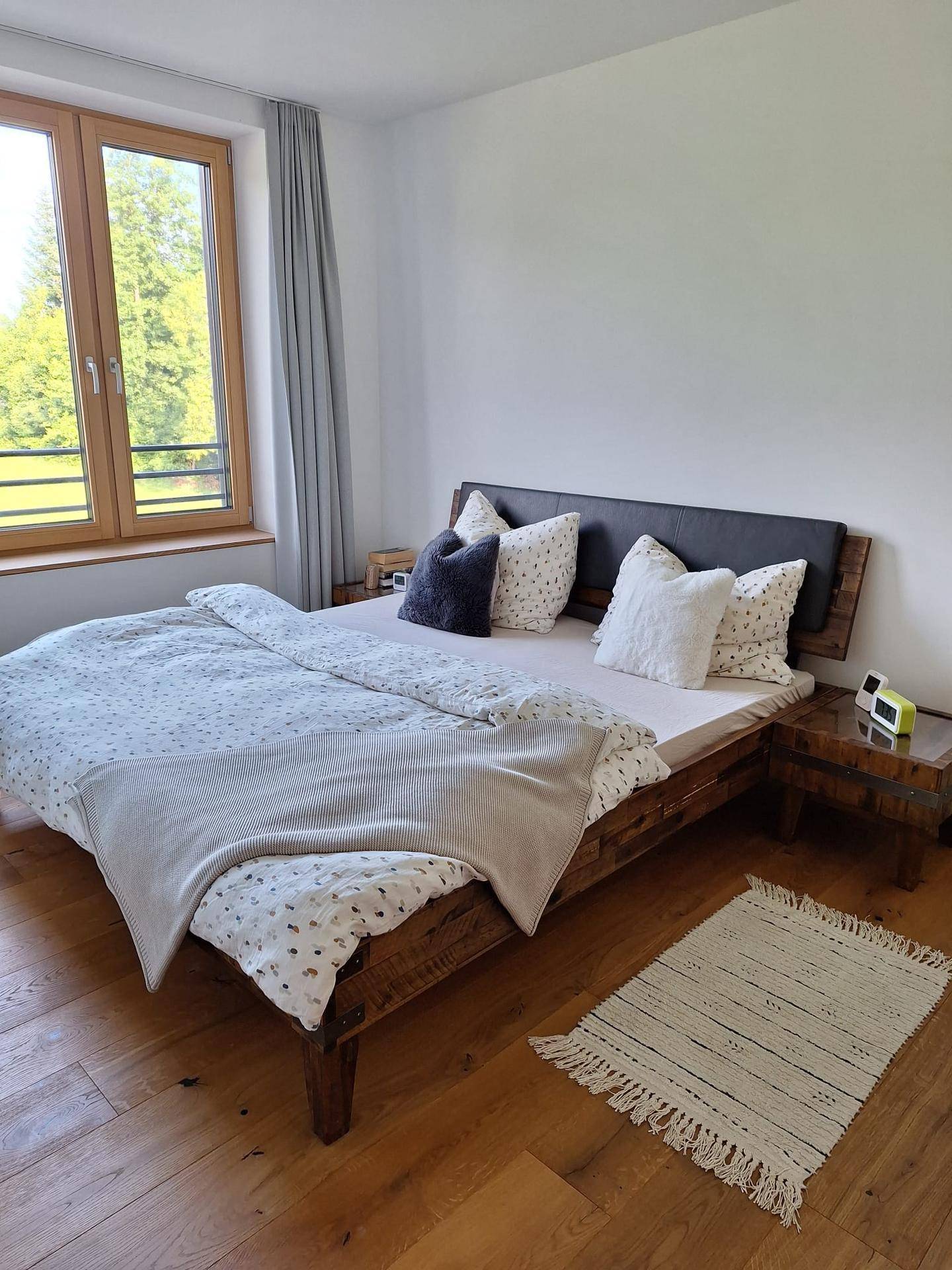 Gemütliches Schlafzimmer mit Holzbett, Parkettboden und Fenster mit Blick ins Grüne.