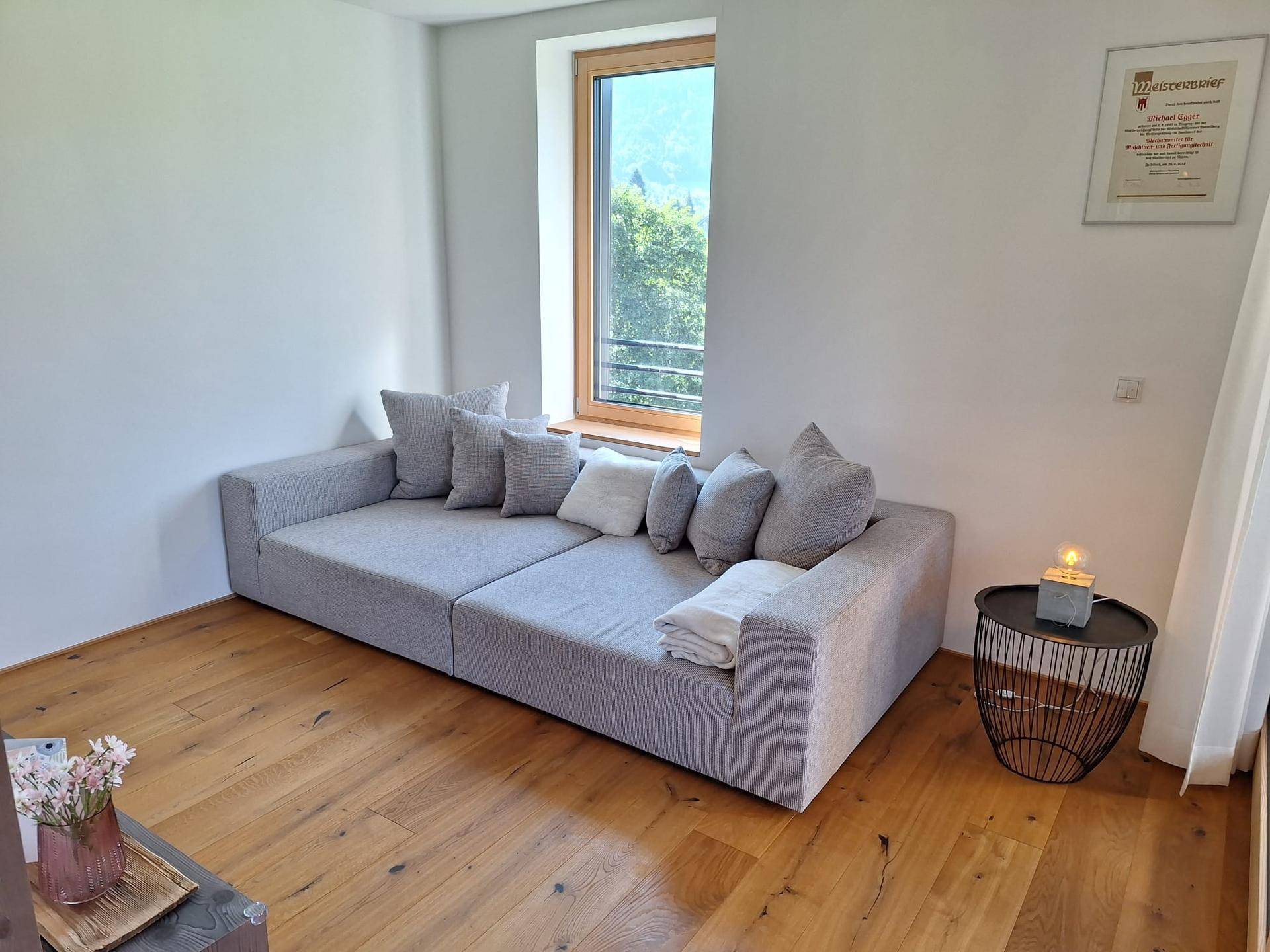 Helles Wohnzimmer mit großem, modernem Sofa und Blick auf die umliegende Landschaft und Berge.