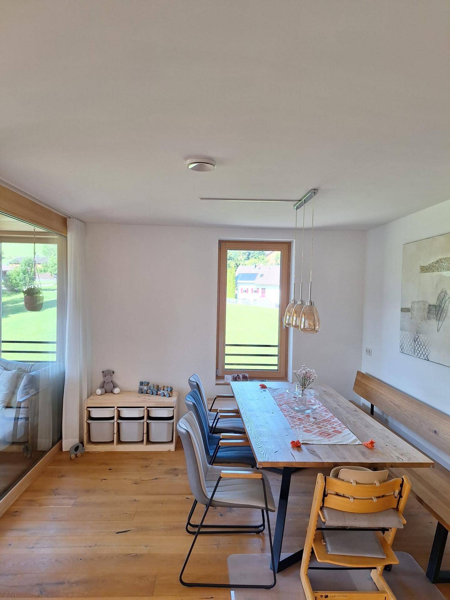Heller Essbereich mit Holztisch, Sitzbank und Blick ins Grüne durch große Fenster.
