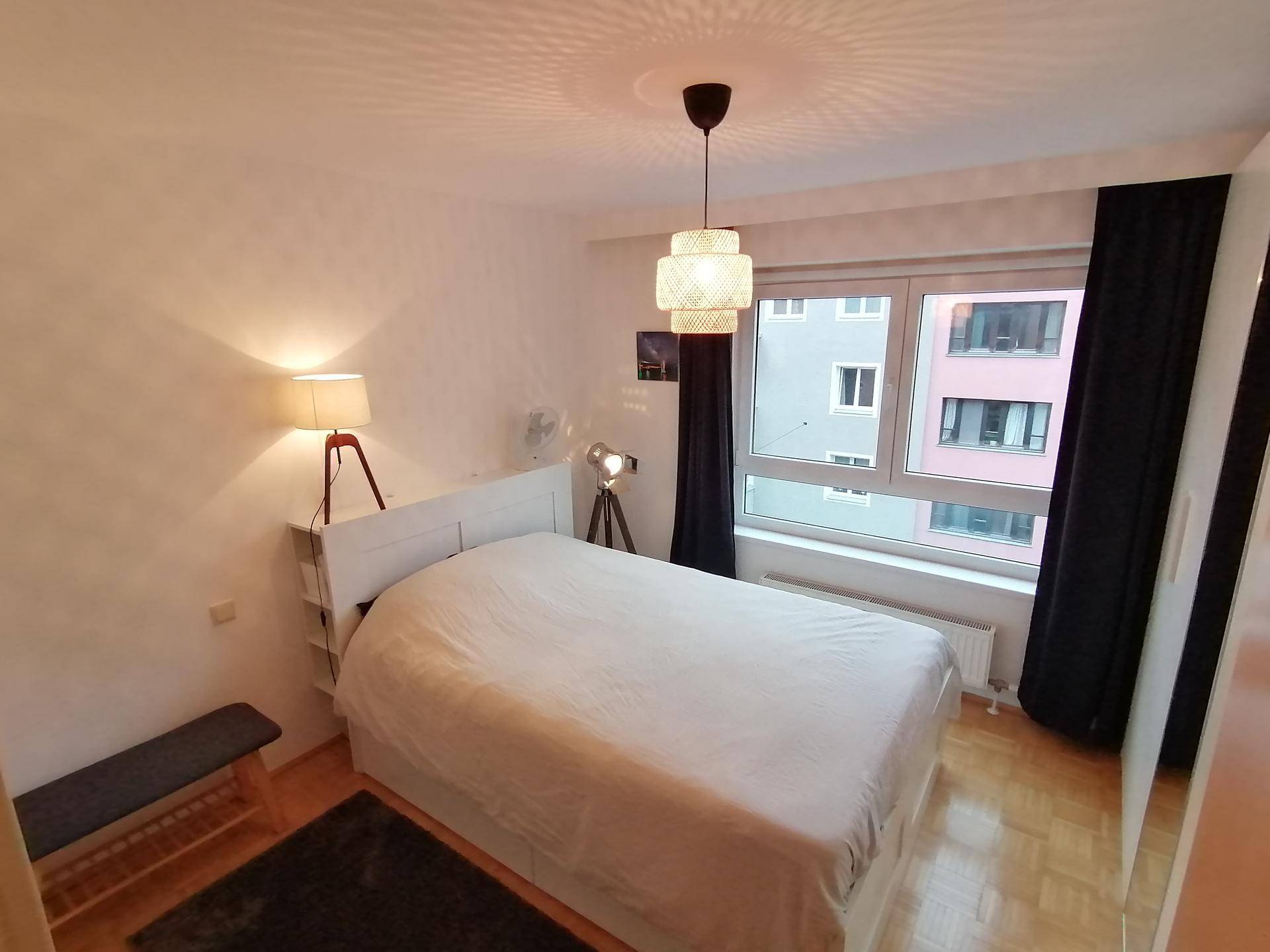 Helles Schlafzimmer mit großem Fenster, Doppelbett und Nachttischlampen.