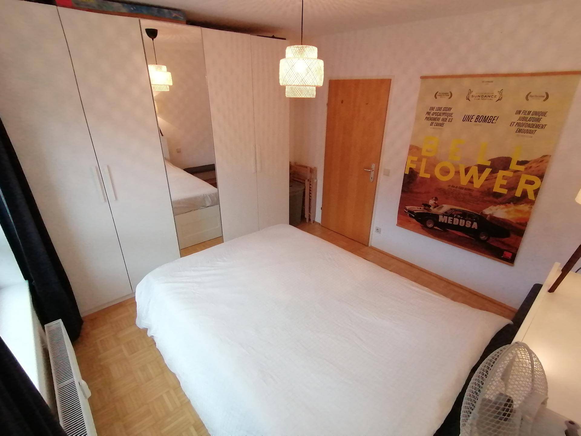 Schlafzimmer mit Doppelbett, weißen Kleiderschränken und Parkettboden.